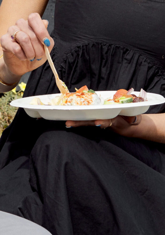 woman eating lunch outdoors with wooden cutlery and sugarcane plate.