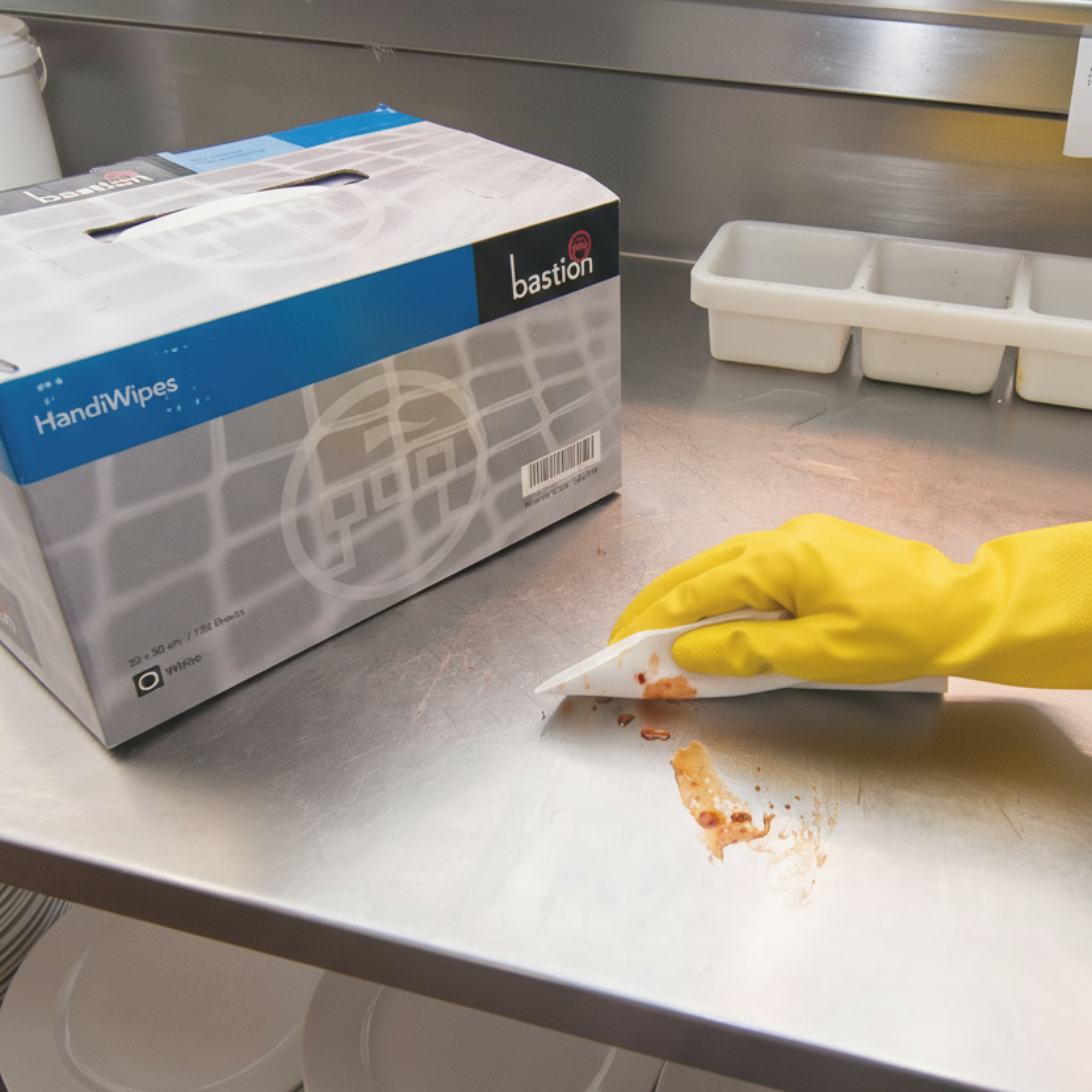 Box of Bastion handi wipes being used on stainless steel bench with reusable household gloves.