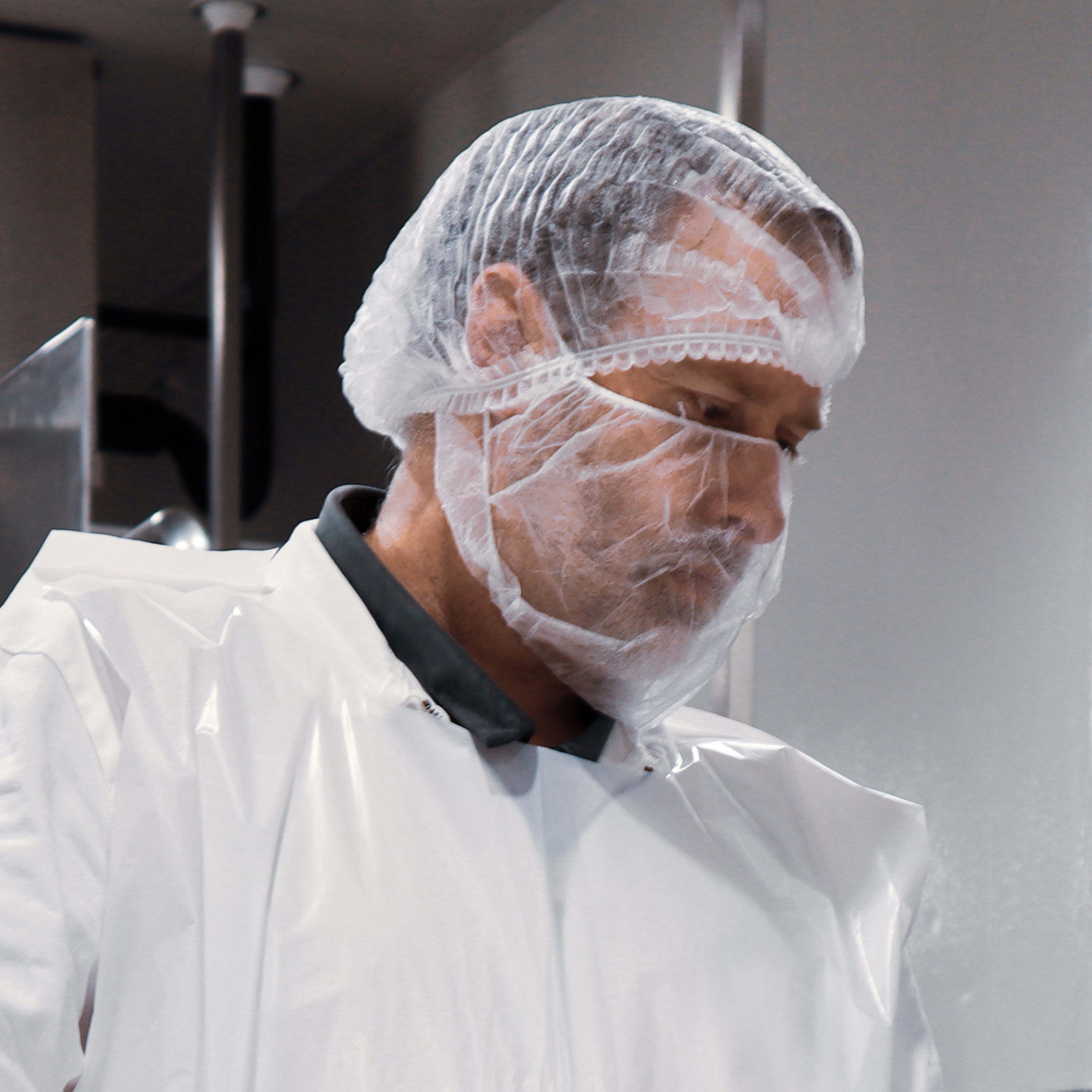 man wearing double loop beard protector, white clip hat and sleeveless white smock.