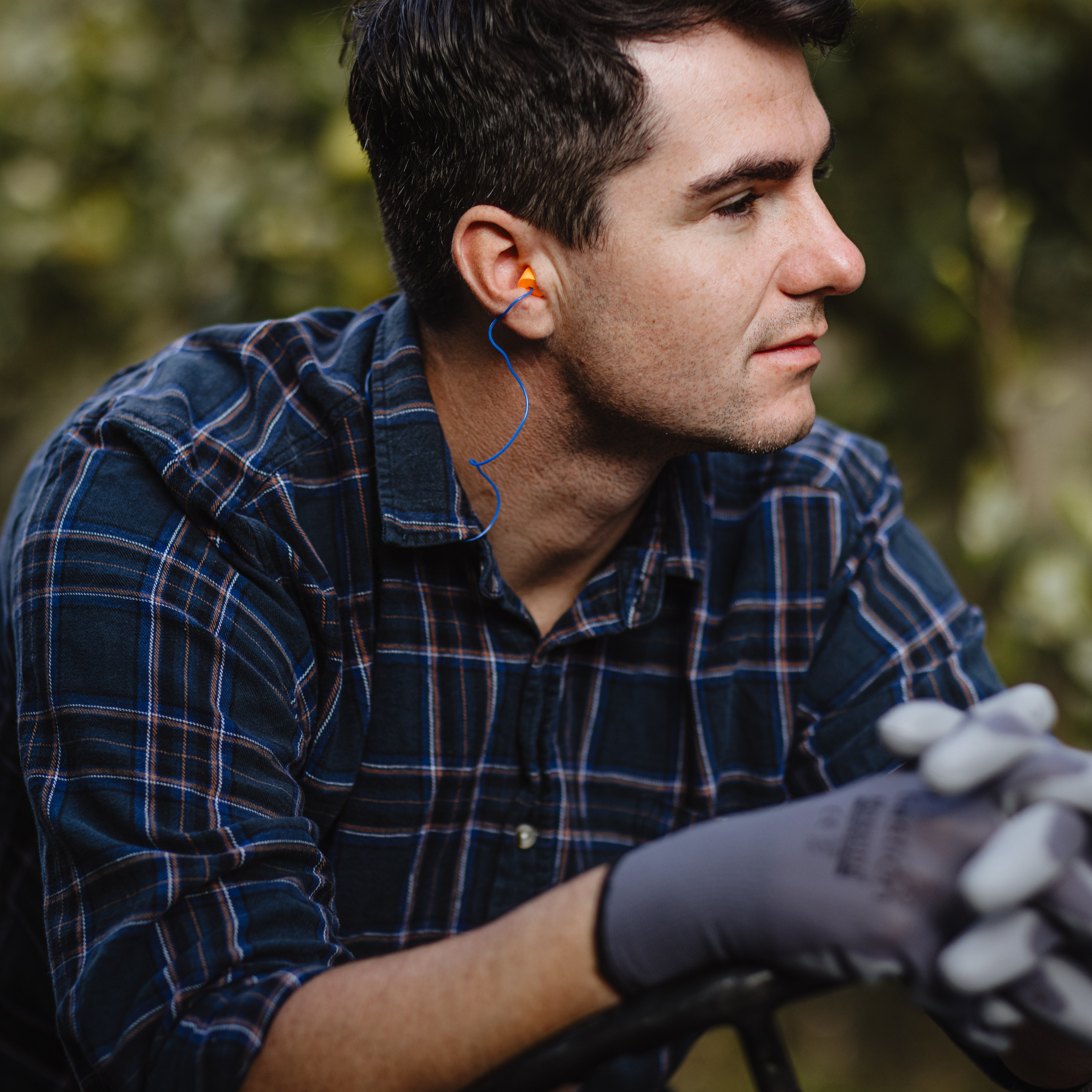 man in orchard wearing corded ear plugs and wearing work gloves