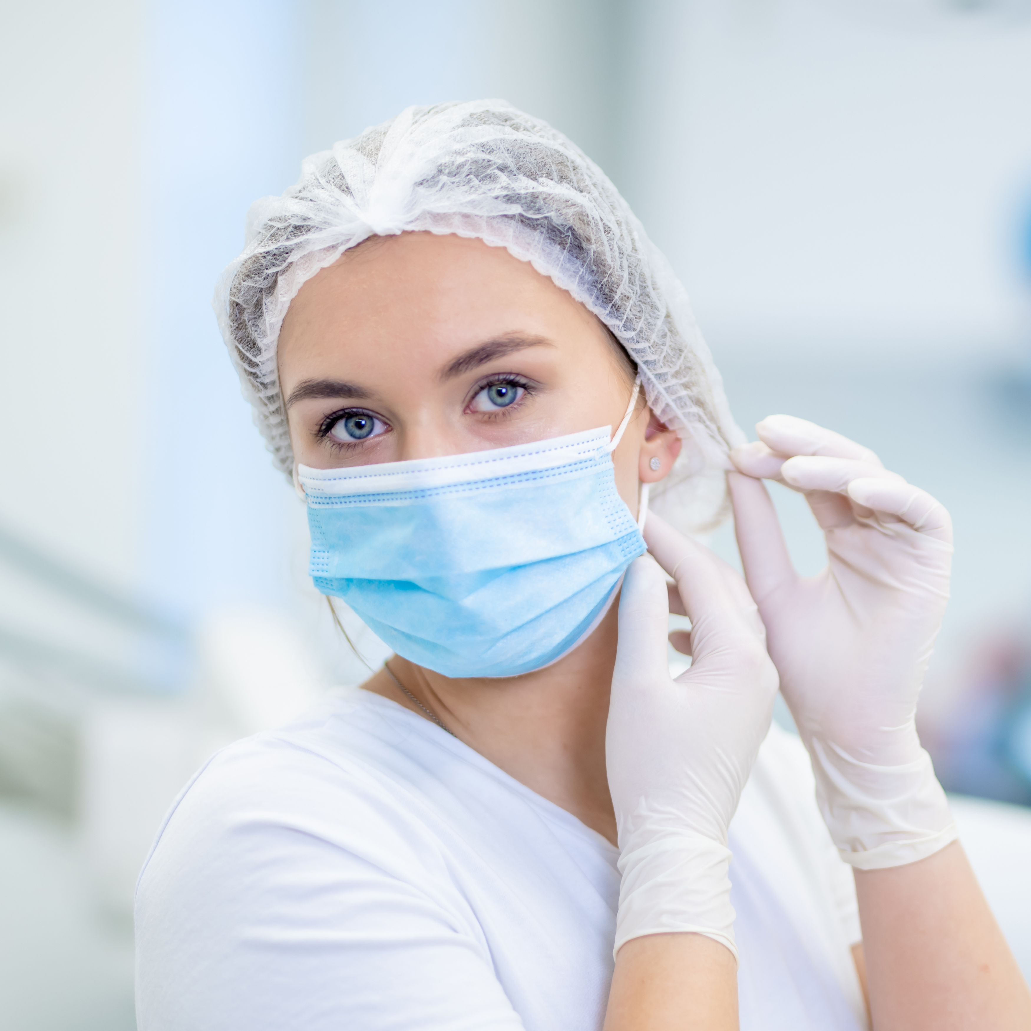 whit shirted female wearing white gloves and mask tucking hair into clip hat