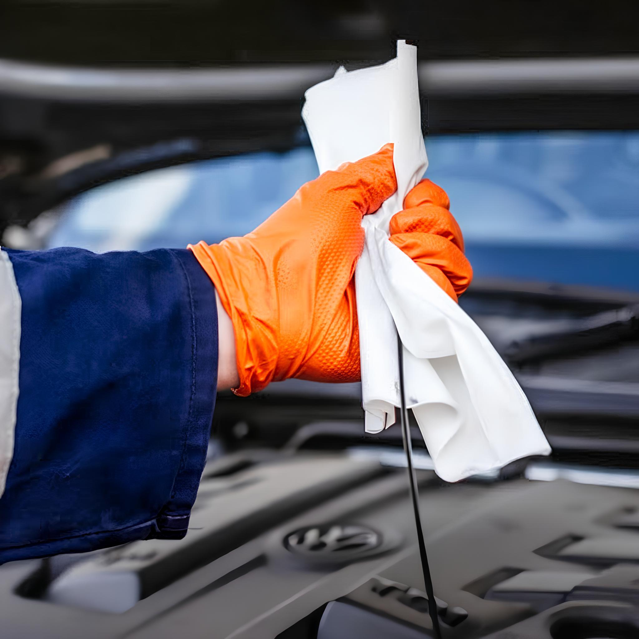 A mechanic is cleaning a dipstick, wearing an orange nitrile glove.
