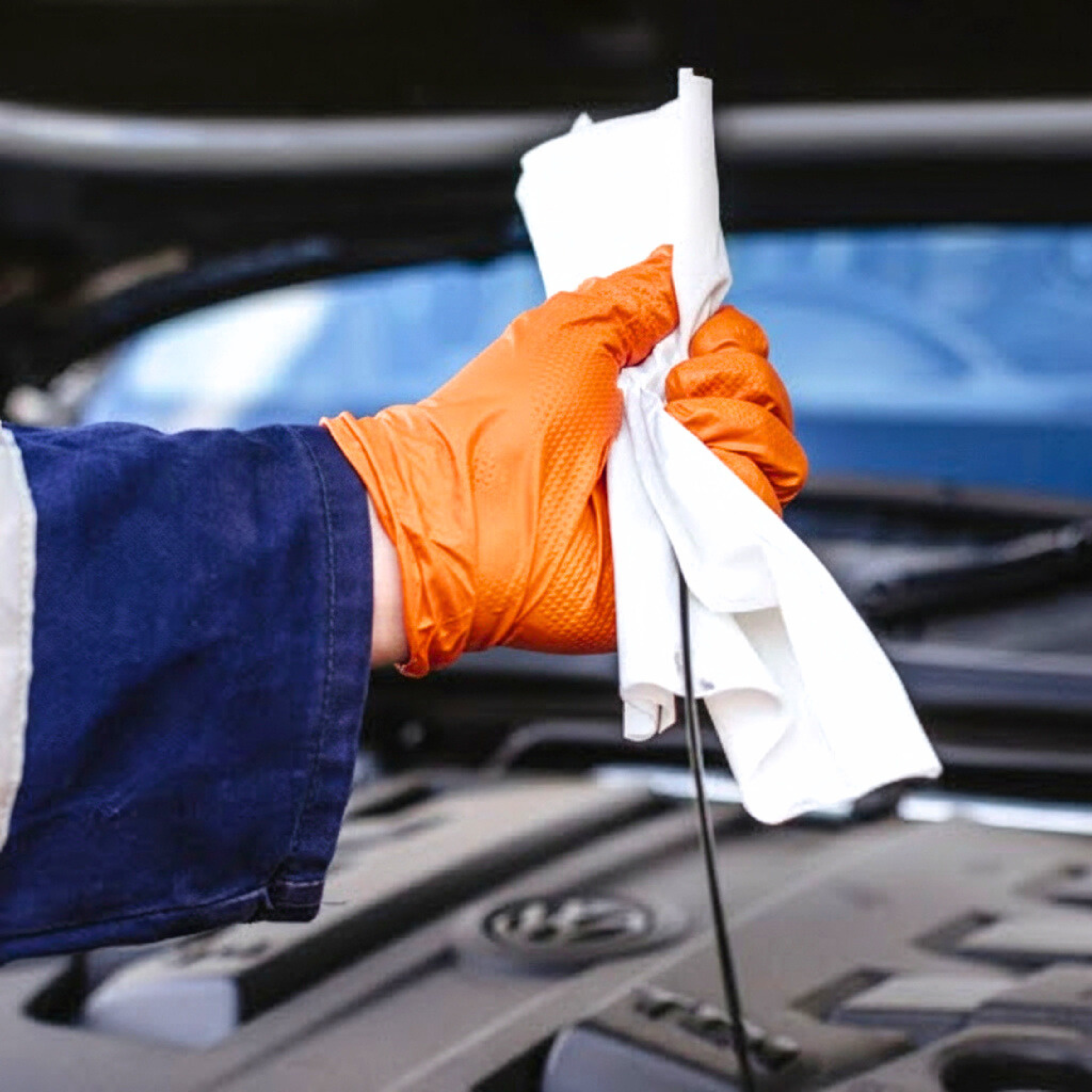 A mechanic is cleaning a dipstick, wearing an orange nitrile glove.