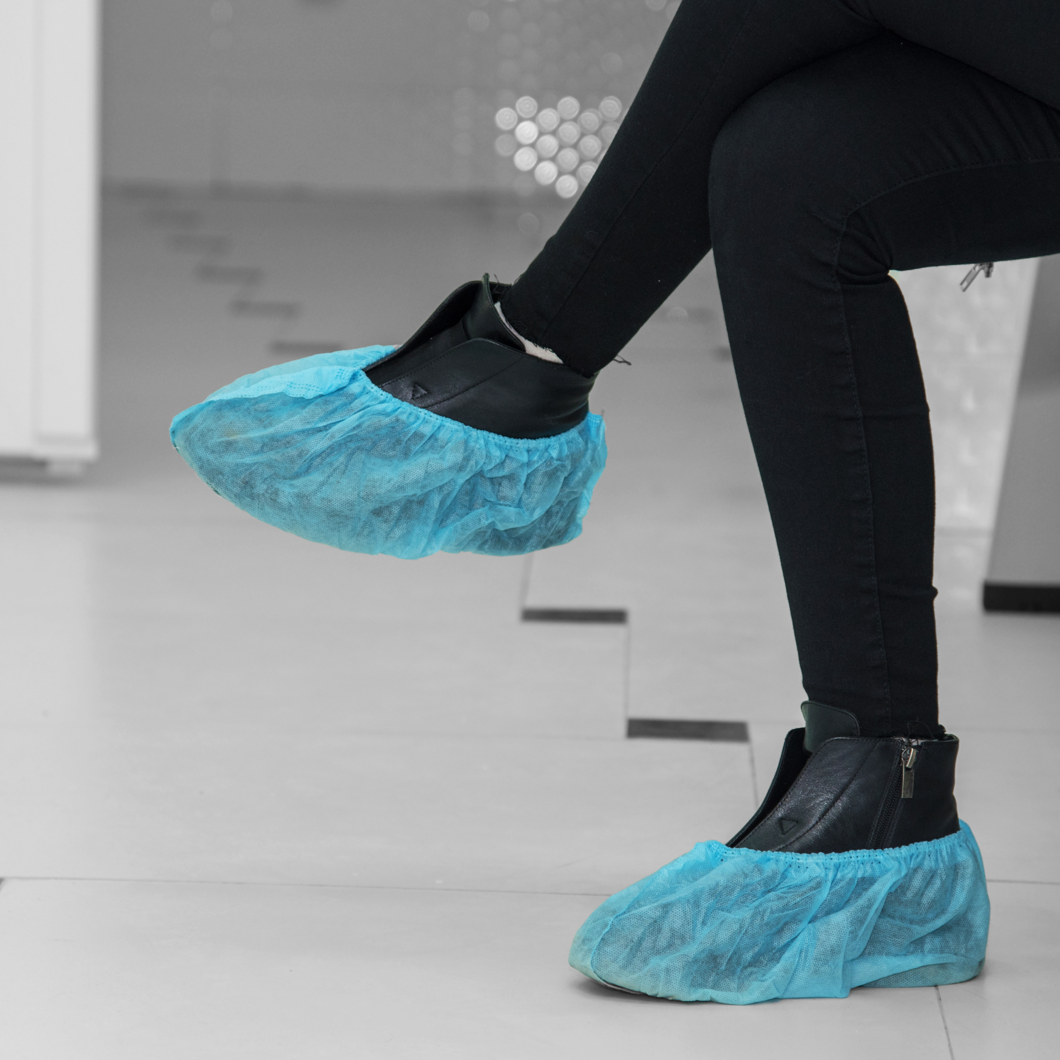 A lady wearing blue overshoes is sitting cross-legged in a clean room.