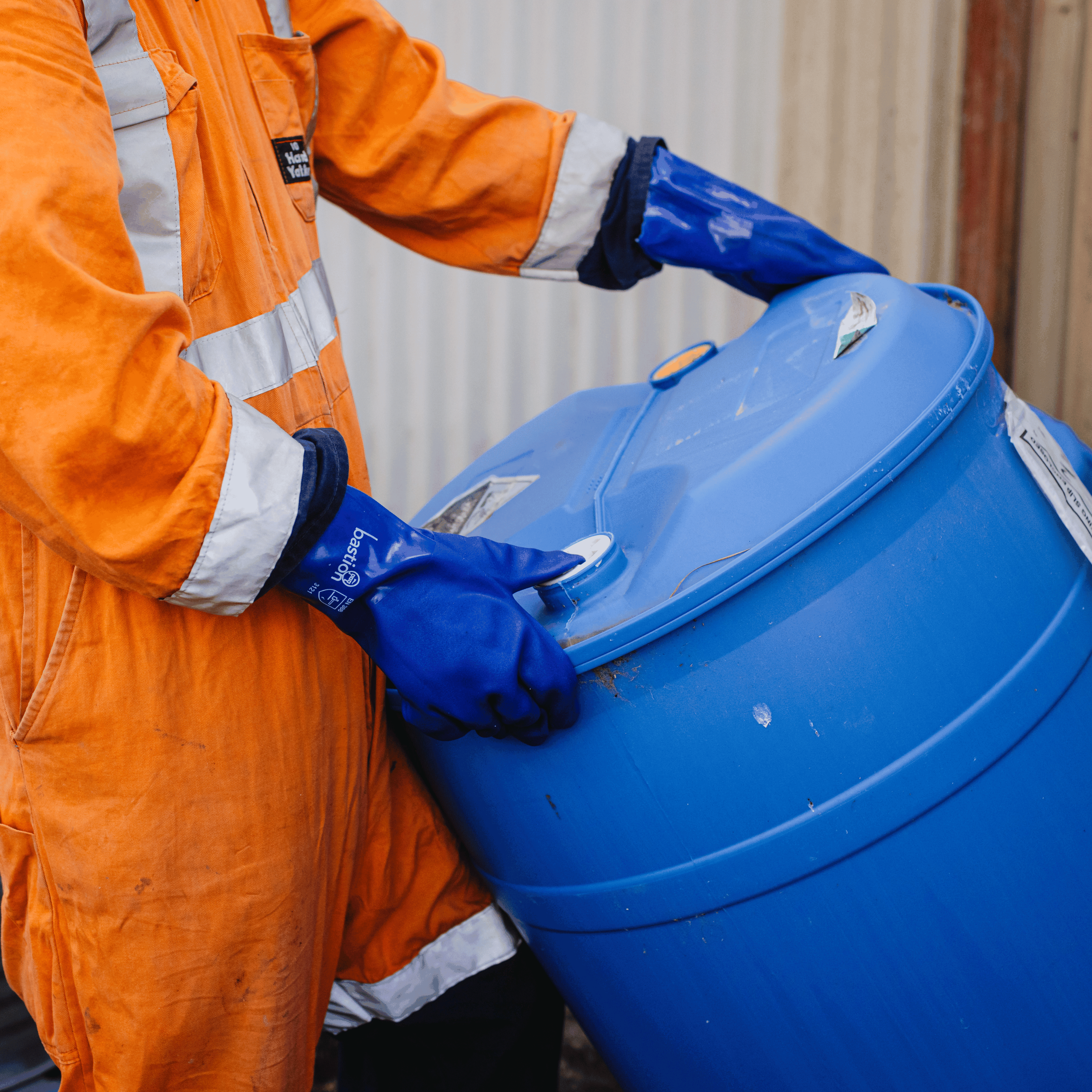 A worker moving a Blue plastic drum wearing Hi-Vis overalls and Bastion PVC Blue Gloves