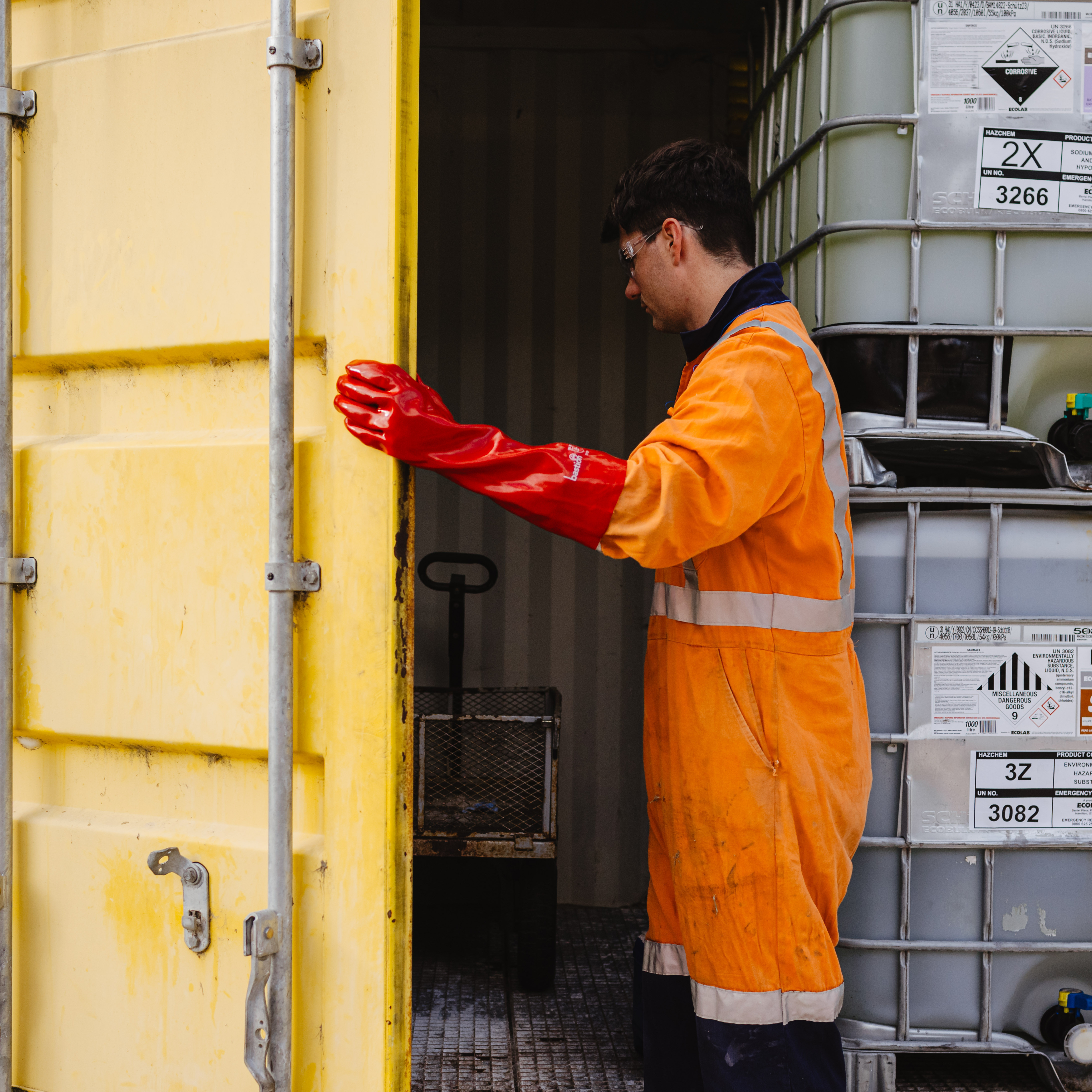A worker going into a container filled with chemicals, wearing Hi-Vis overalls and Bastion PVC Red 45cm Cuff Gloves