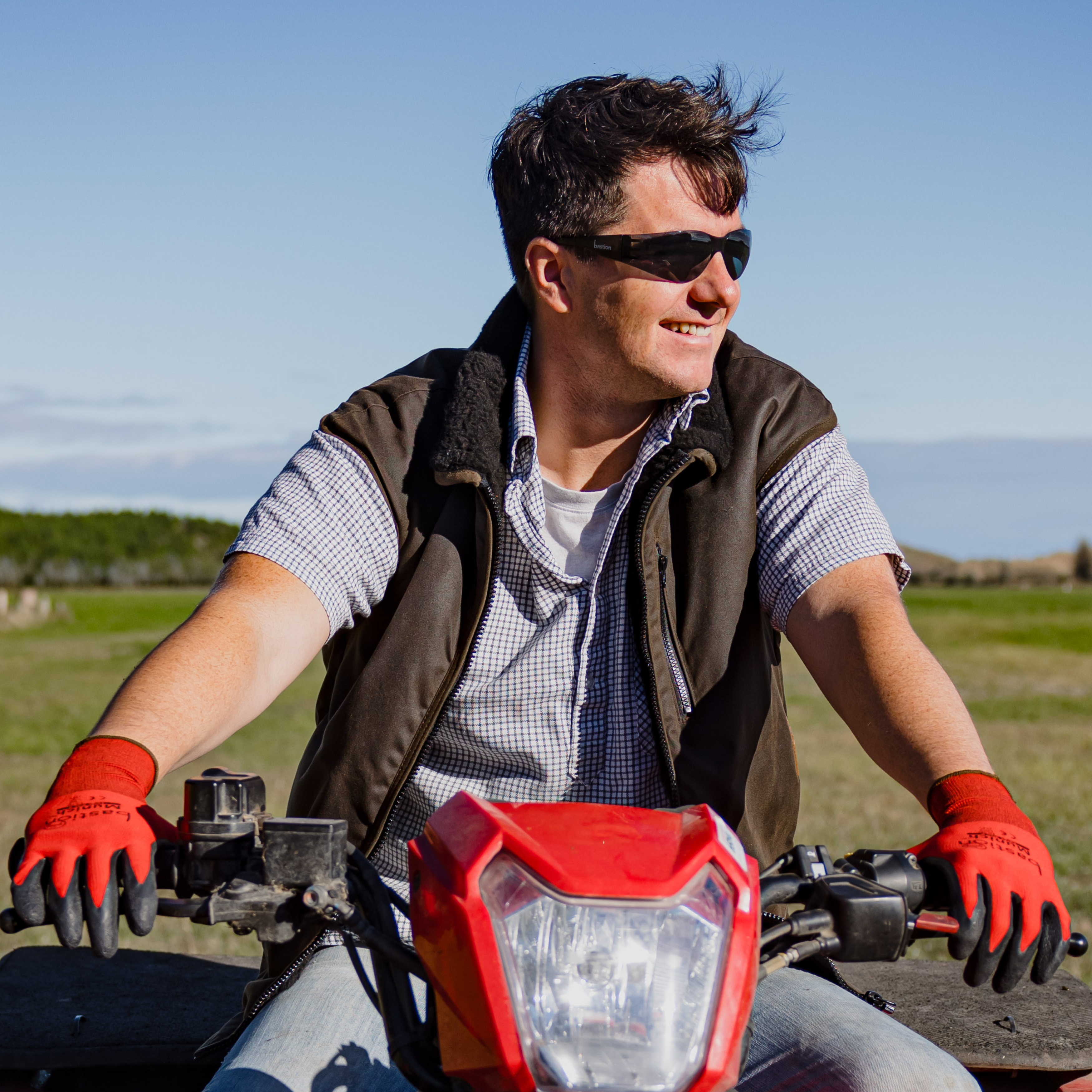 Farmer riding 4-wheeler, wearing Bastion Smoke Safety Glasses and Munich Gloves