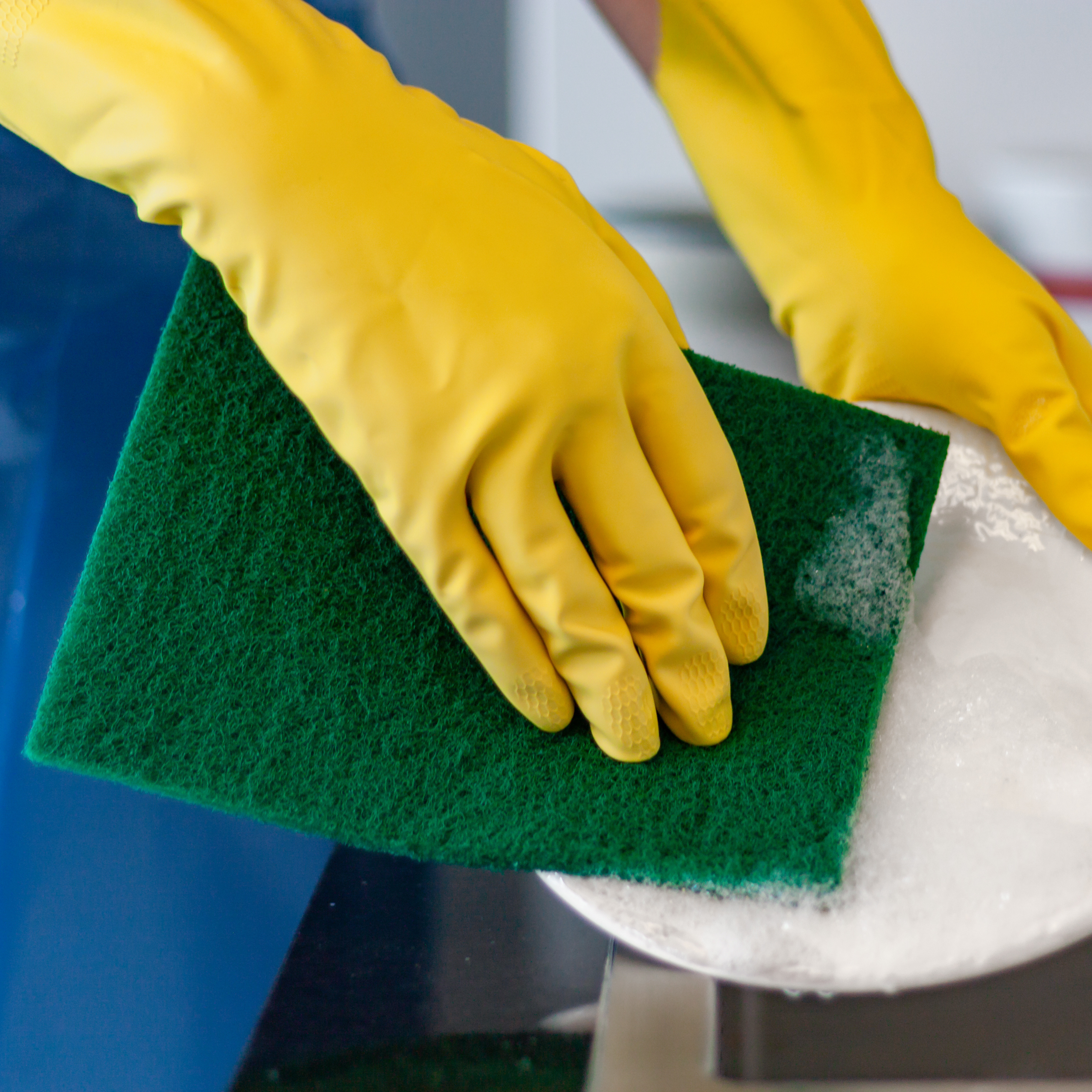 person wearing yellow silverlined gloves using scouring pad on plate