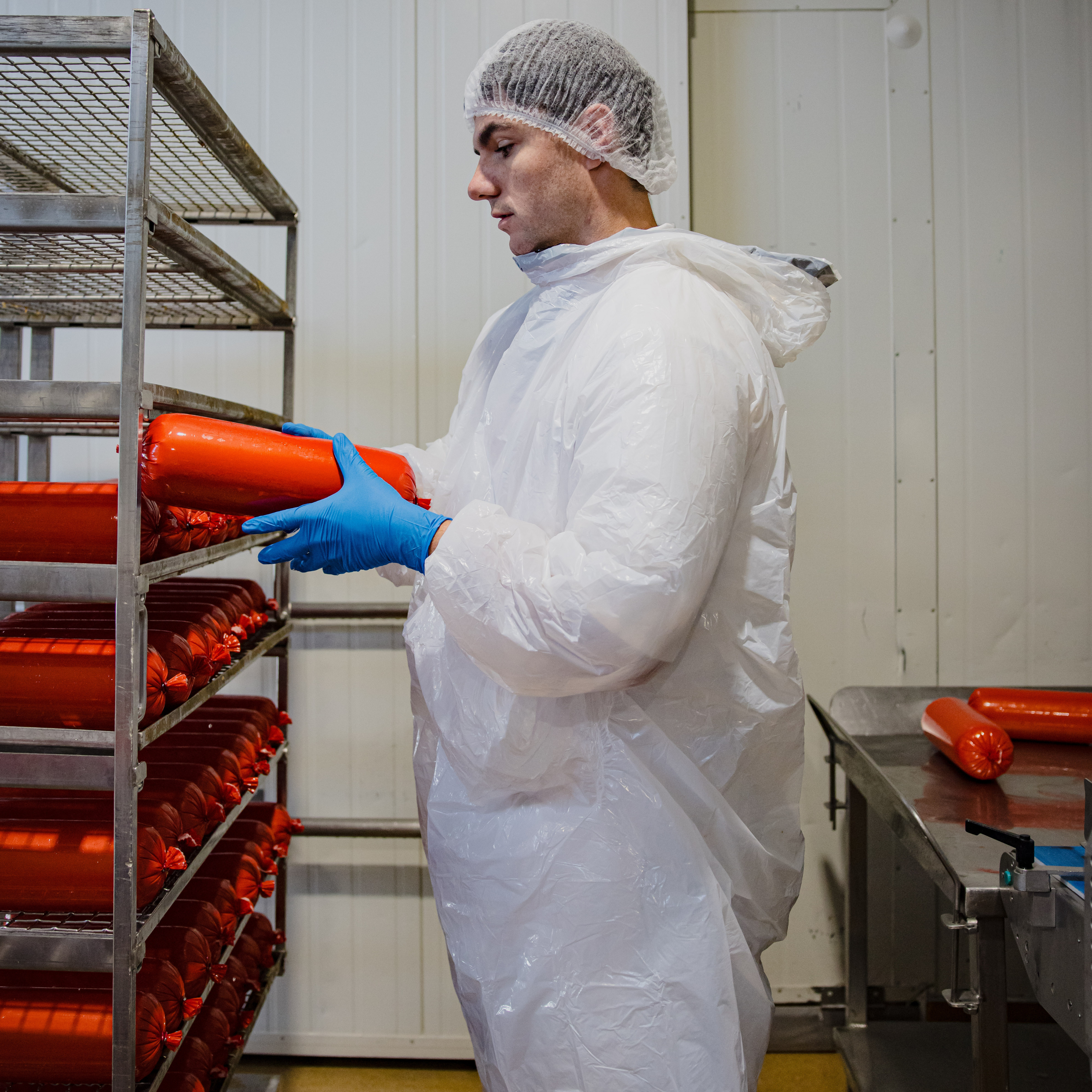meat working wearing white hooded long sleeve splash jacket, blue nitrile gloves and white hairnet.