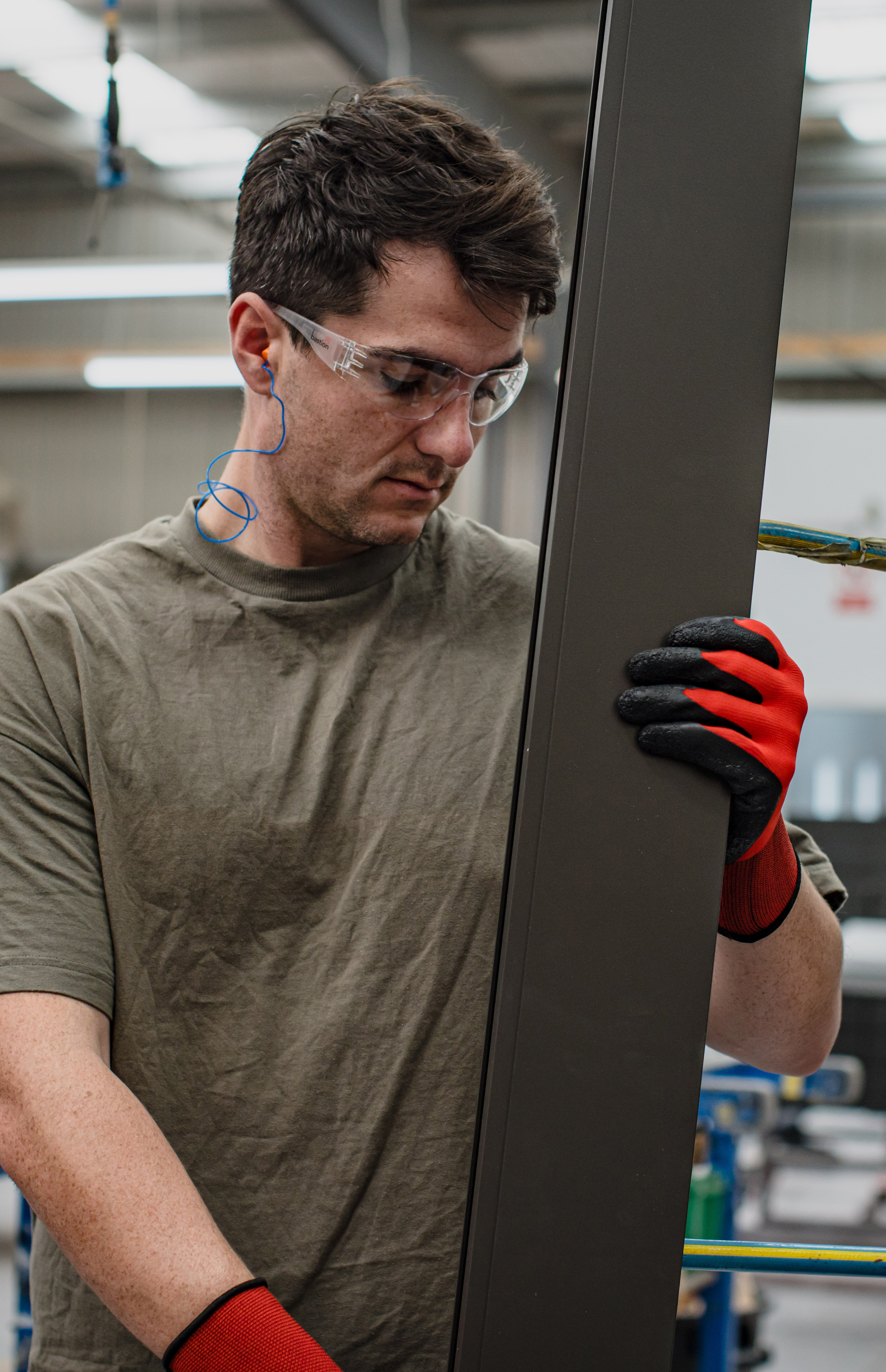 man wearing short sleeved shirt,  red protective gloves, ear plugs, and safety glasses holding plank