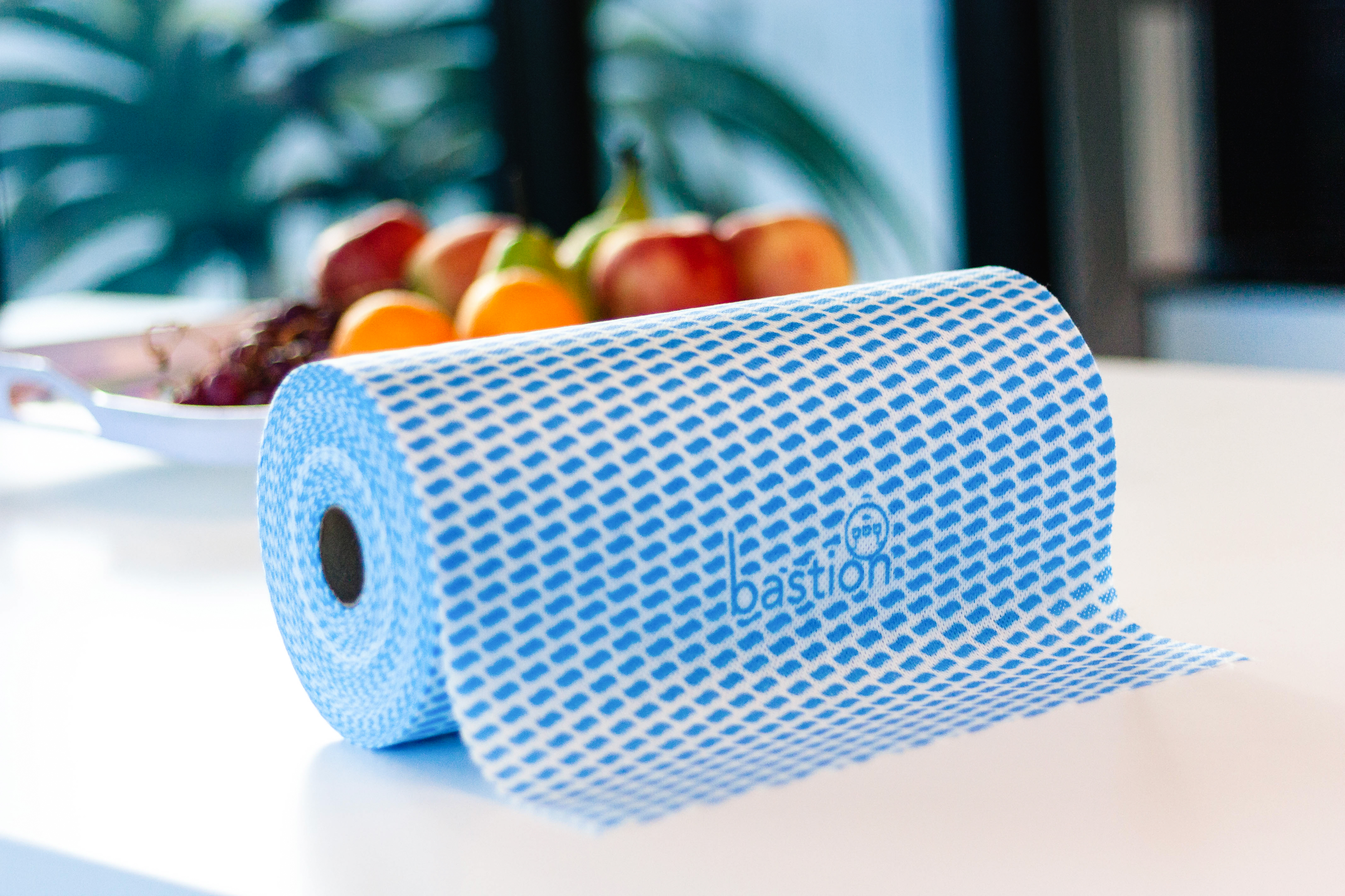 Blue Bastion branded dry wipes on a roll displayed on table with fruitbasket in background.