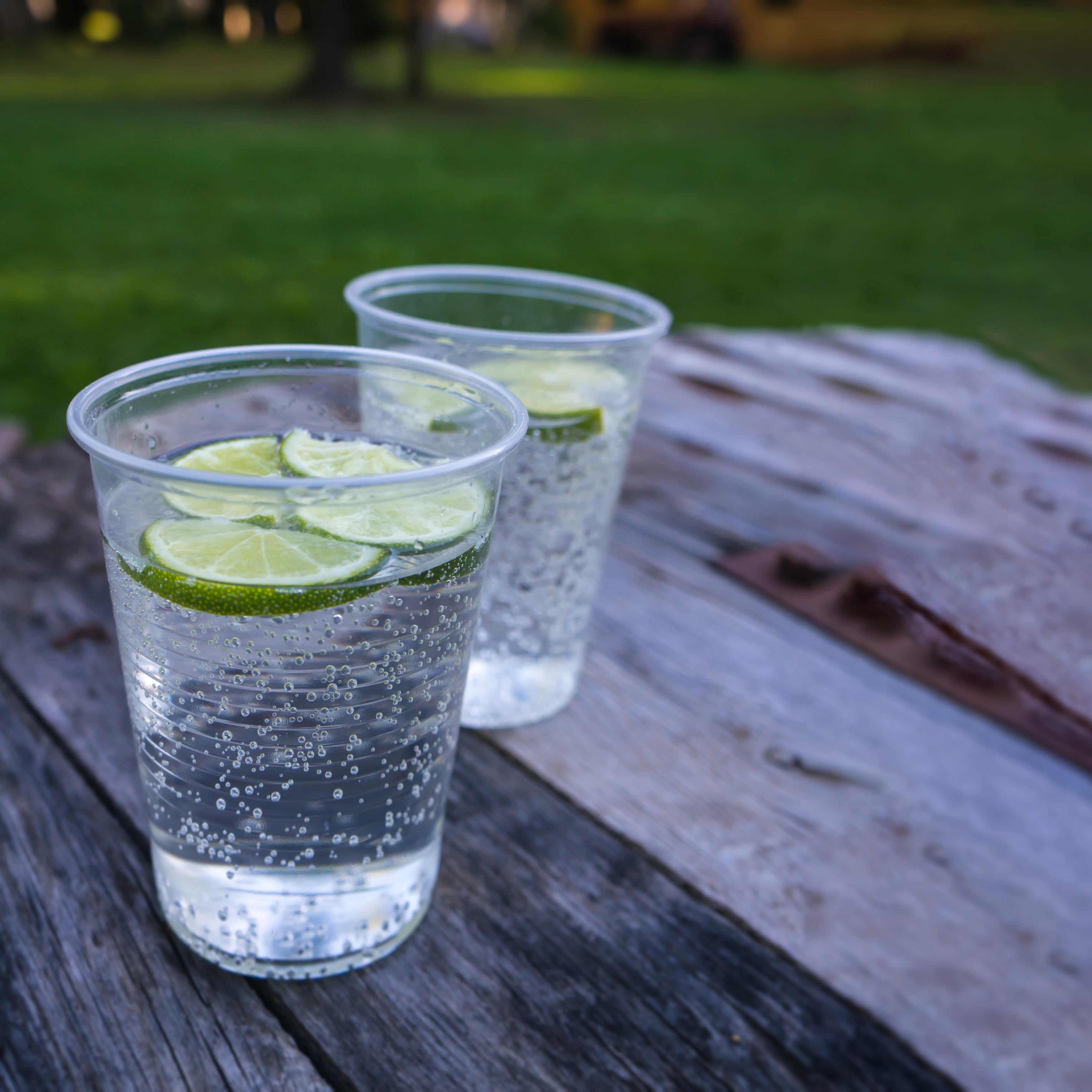 Water cups filled with lemonade, garnished with lime slices, sitting on a picnic bench