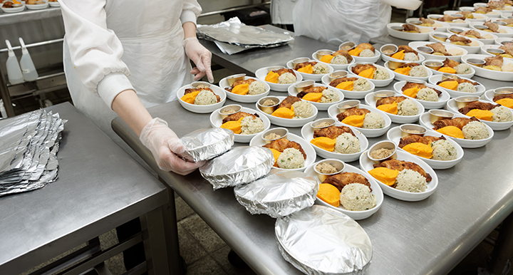 Multiple meals are laid out on a kitchen bench, and a chef is wrapping them with foil.