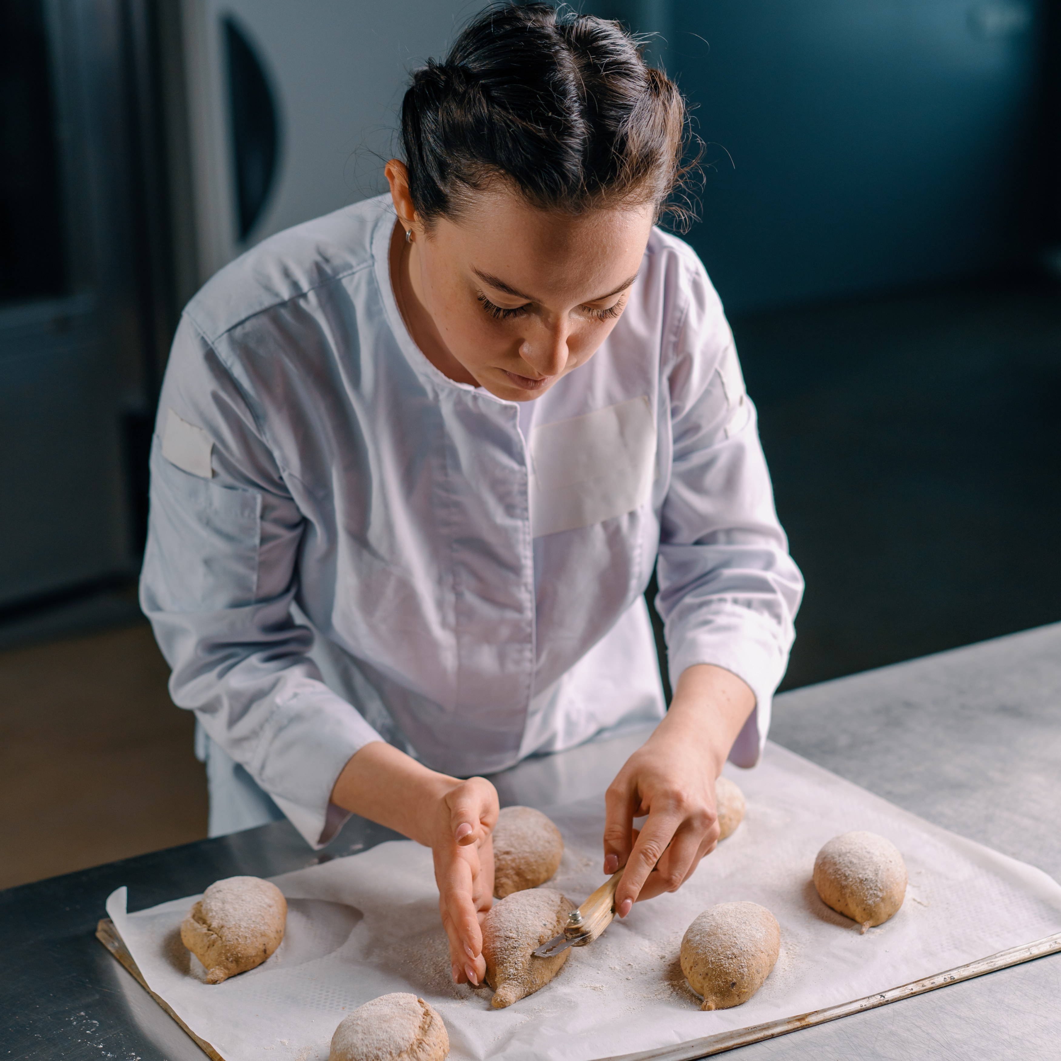 A lady in a commercial kitchen using a greaseproof sheet on her over tray