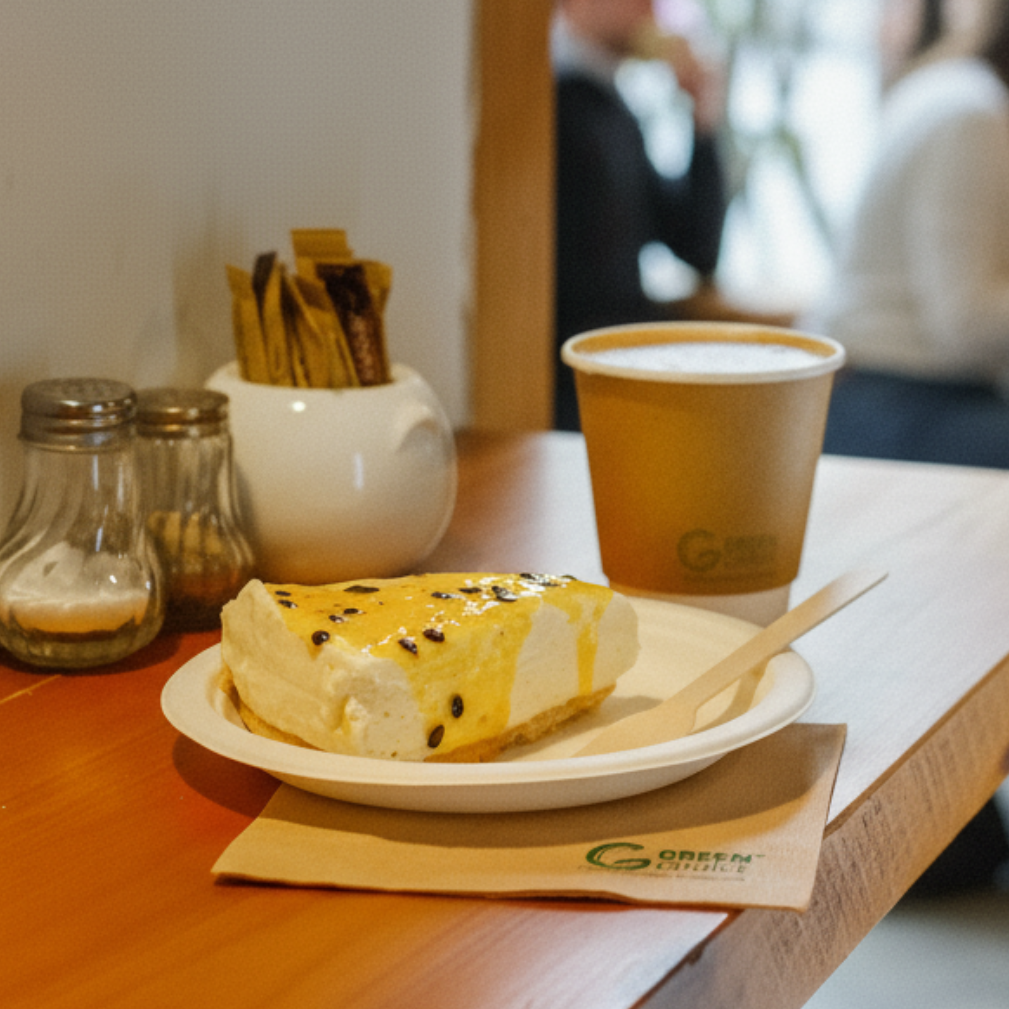 Cheesecake on a sugarcane plate with a coffee in a Green Choice coffee cup sitting on a table at a cafe