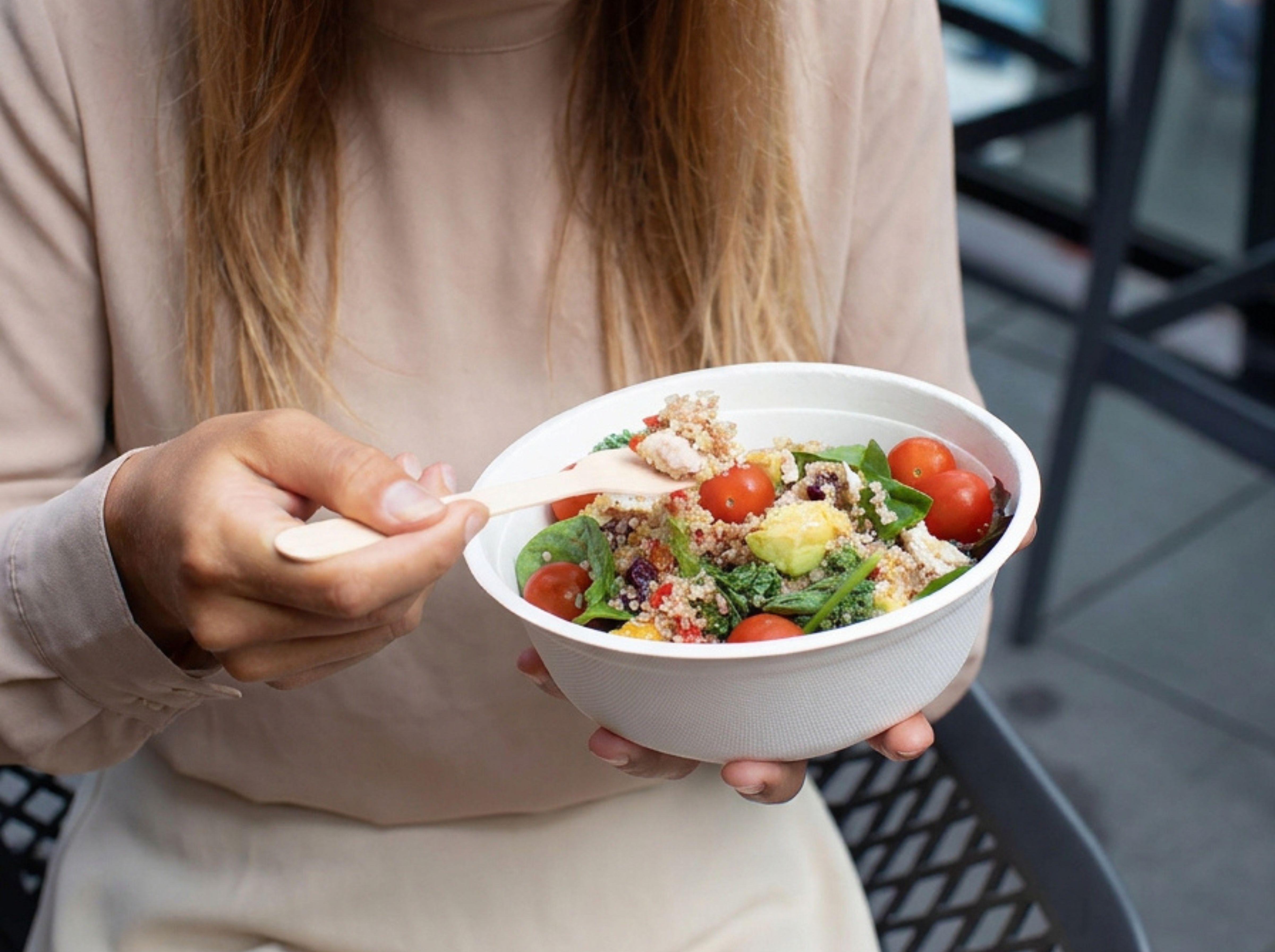 A lady sitting down, enjoying eating a salad from a Green Choice Sugar Cane Bowl