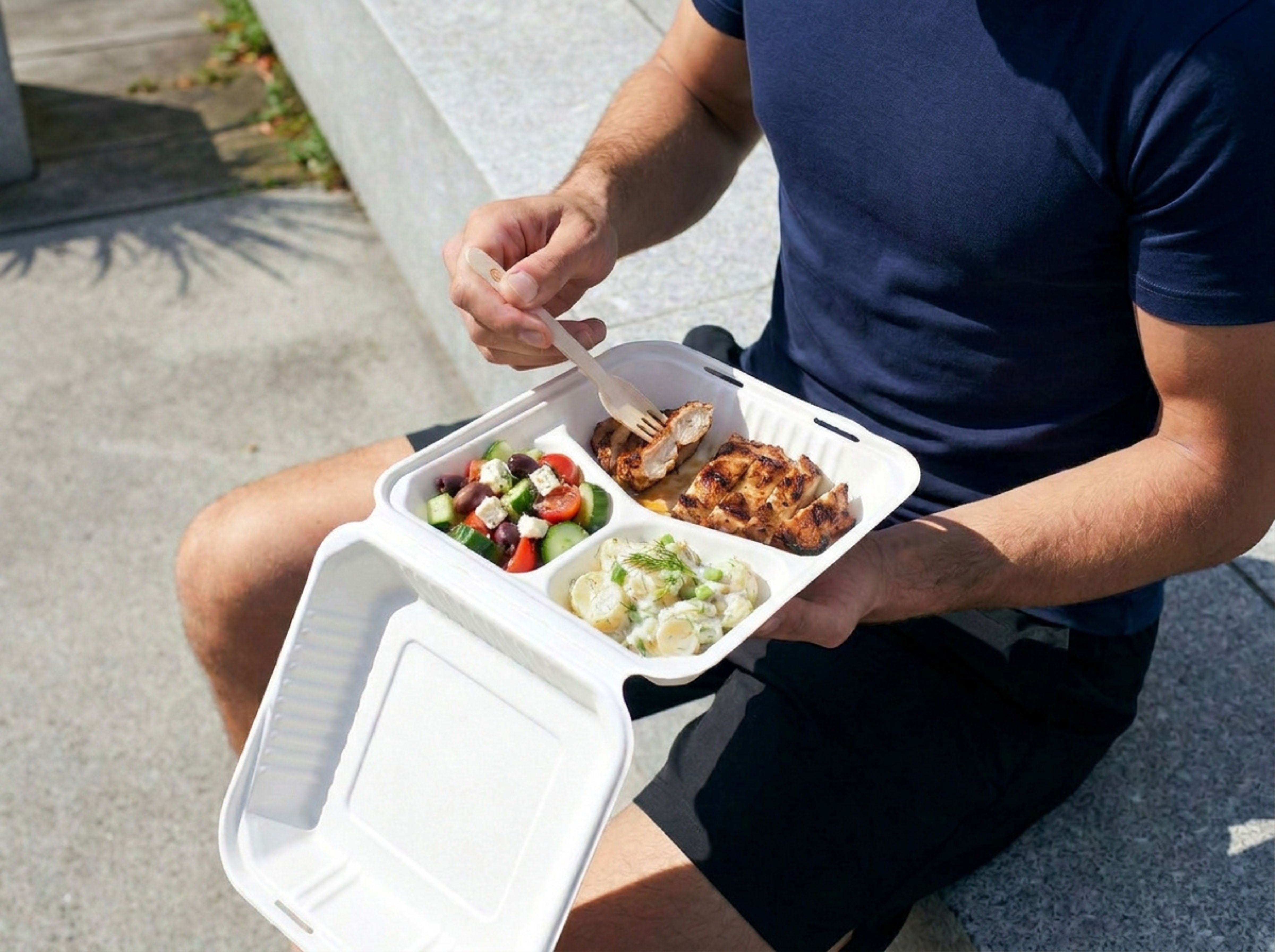 a 3-compartment sugarcane container filled with food sitting on the bench.