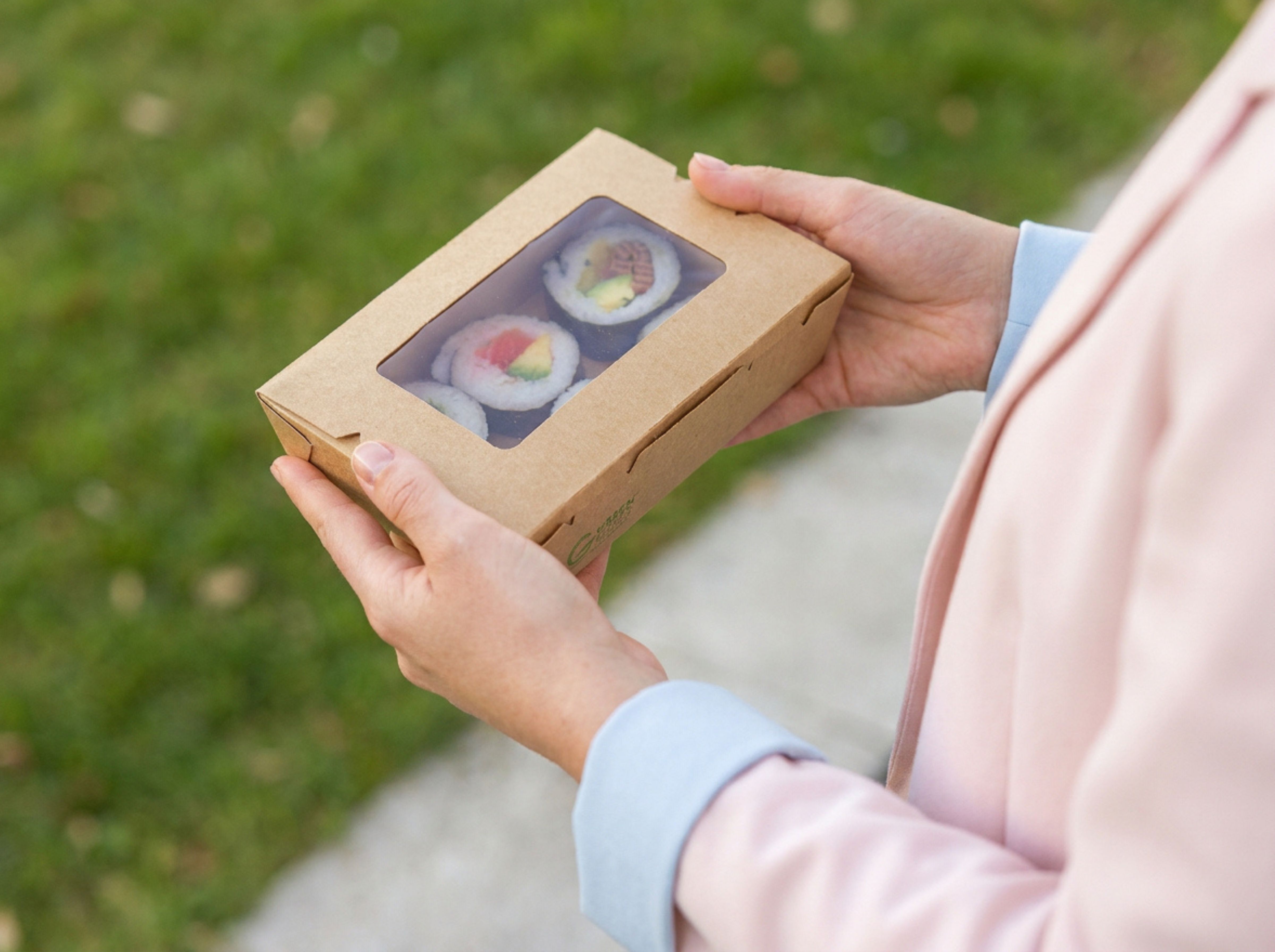 Lady holding a takeaway box with a window. You can see the contents of the sushi inside the Green Choice box