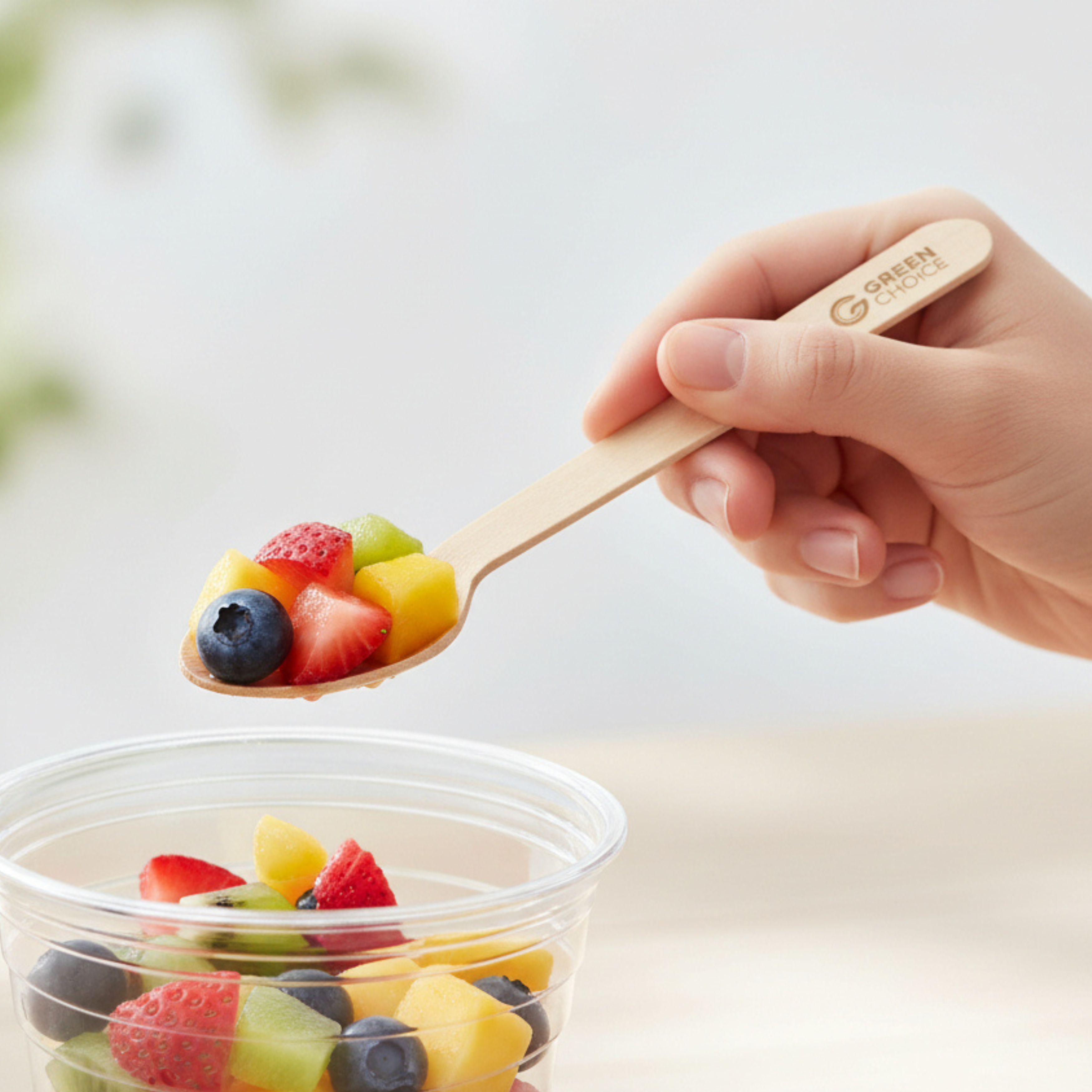 A Green Choice wooden spoon is being used to eat a fresh fruit salad.