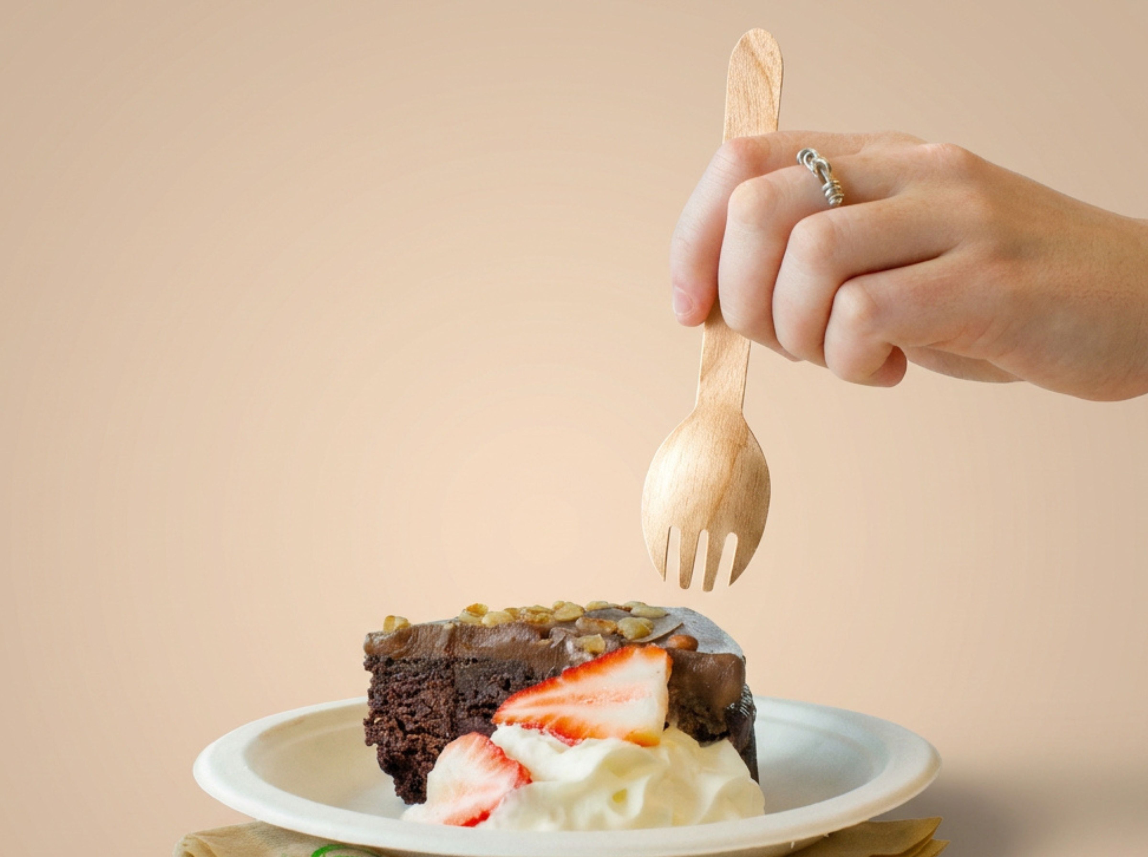 Lady using a spork to eat a slice of chocolate cake with whipped cream and strawberries