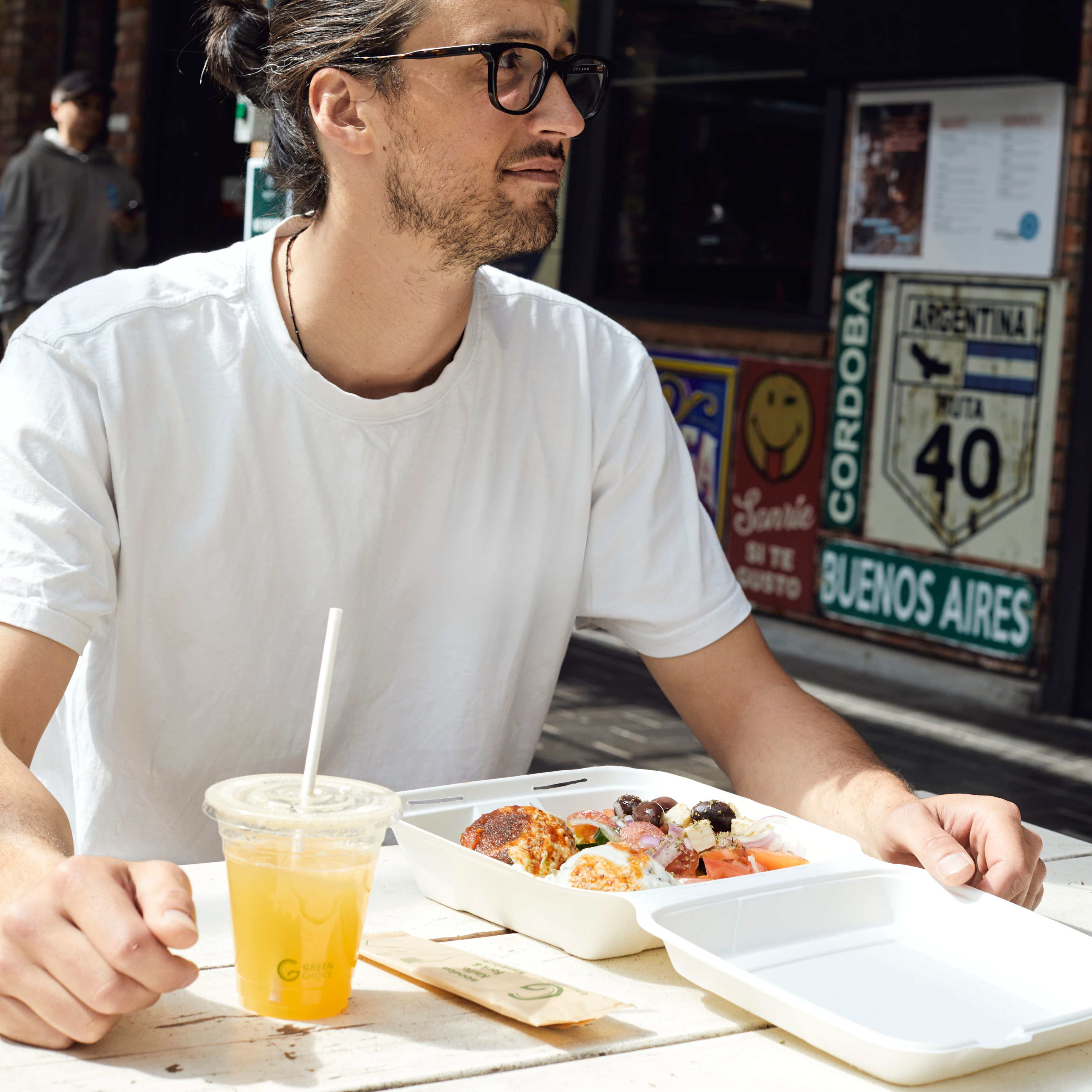 A man sitting down to enjoy his meal in a Green Choice sugarcane clamshell container with a Green Choice Cold cup filled with juice