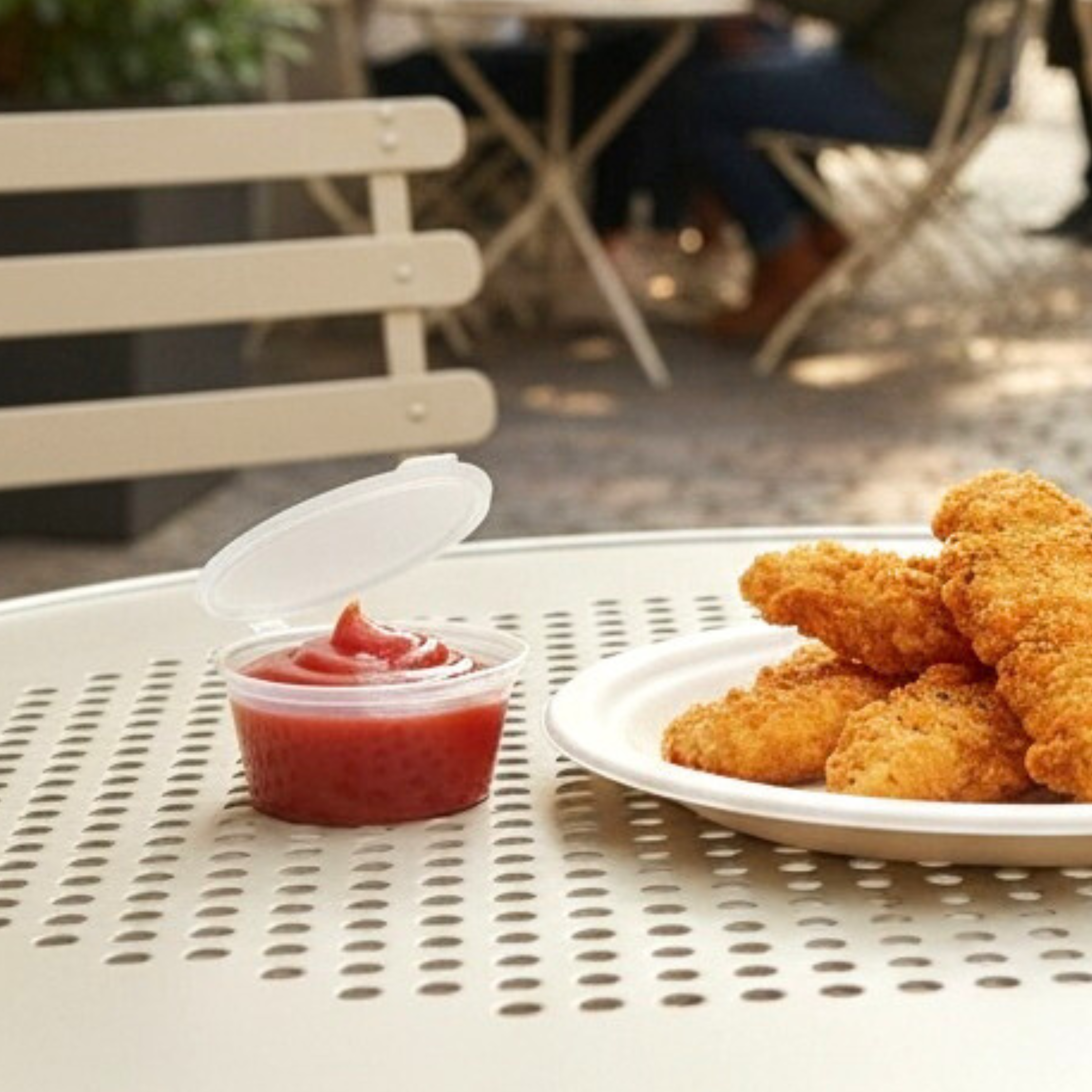 Sauce container filled with tomato sauce sitting on a cafe table next to some chicken