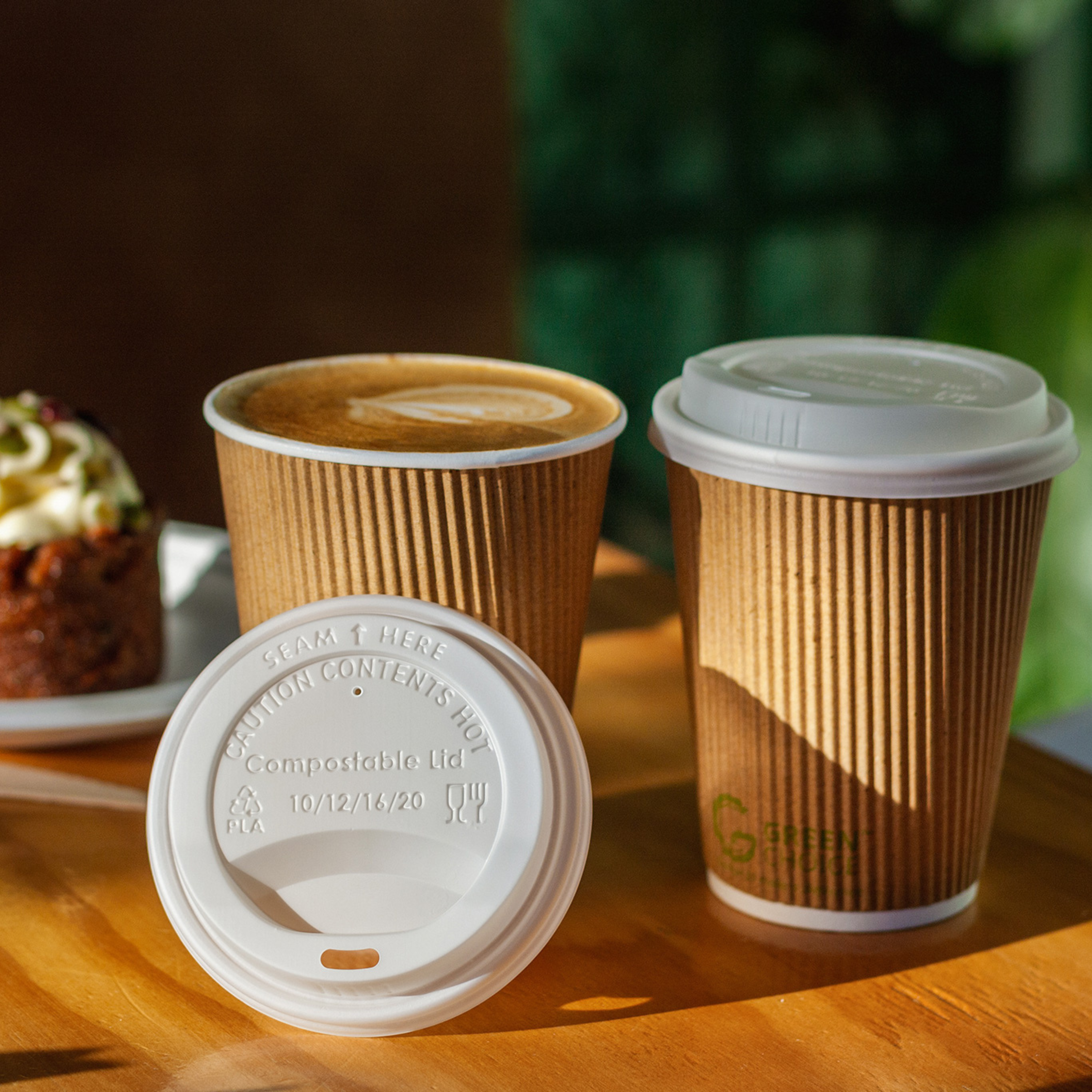A Green Choice CPLA hot cup lid leaning against a Green Choice ripple wall cup