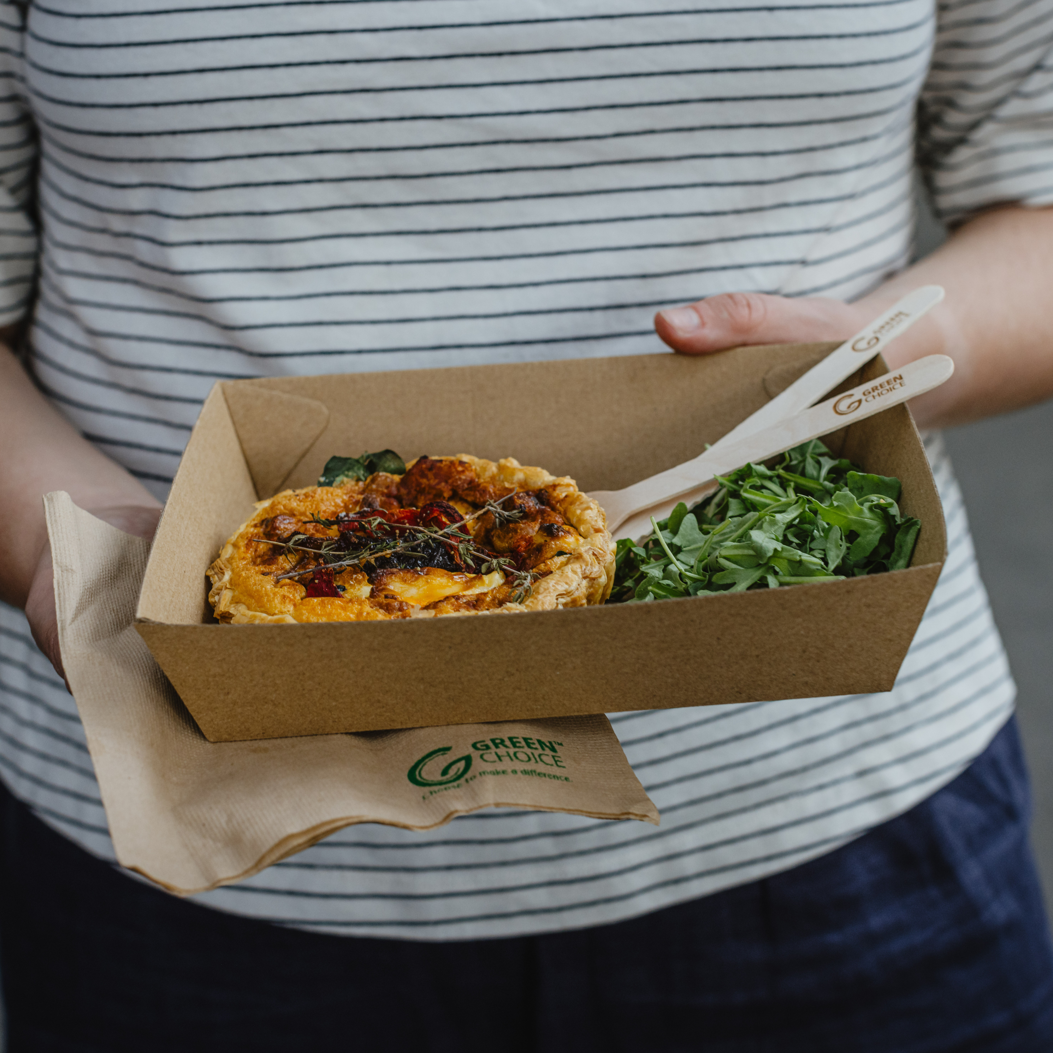 A close-up of someone carrying a Green Choice corrugate tray with a quiche and salad