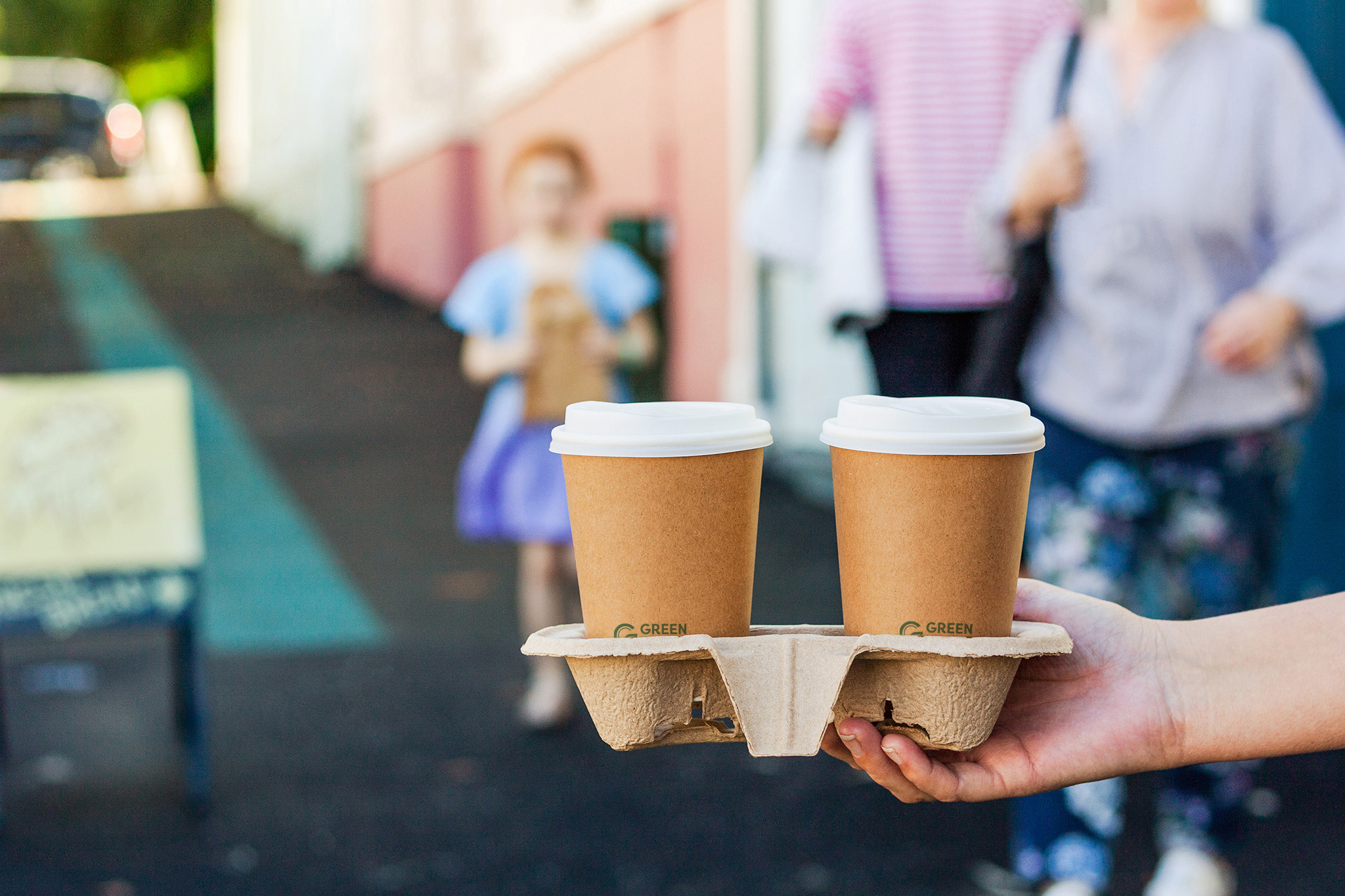 hands holding double cup holder, family out of focus in background. outdoors, summer