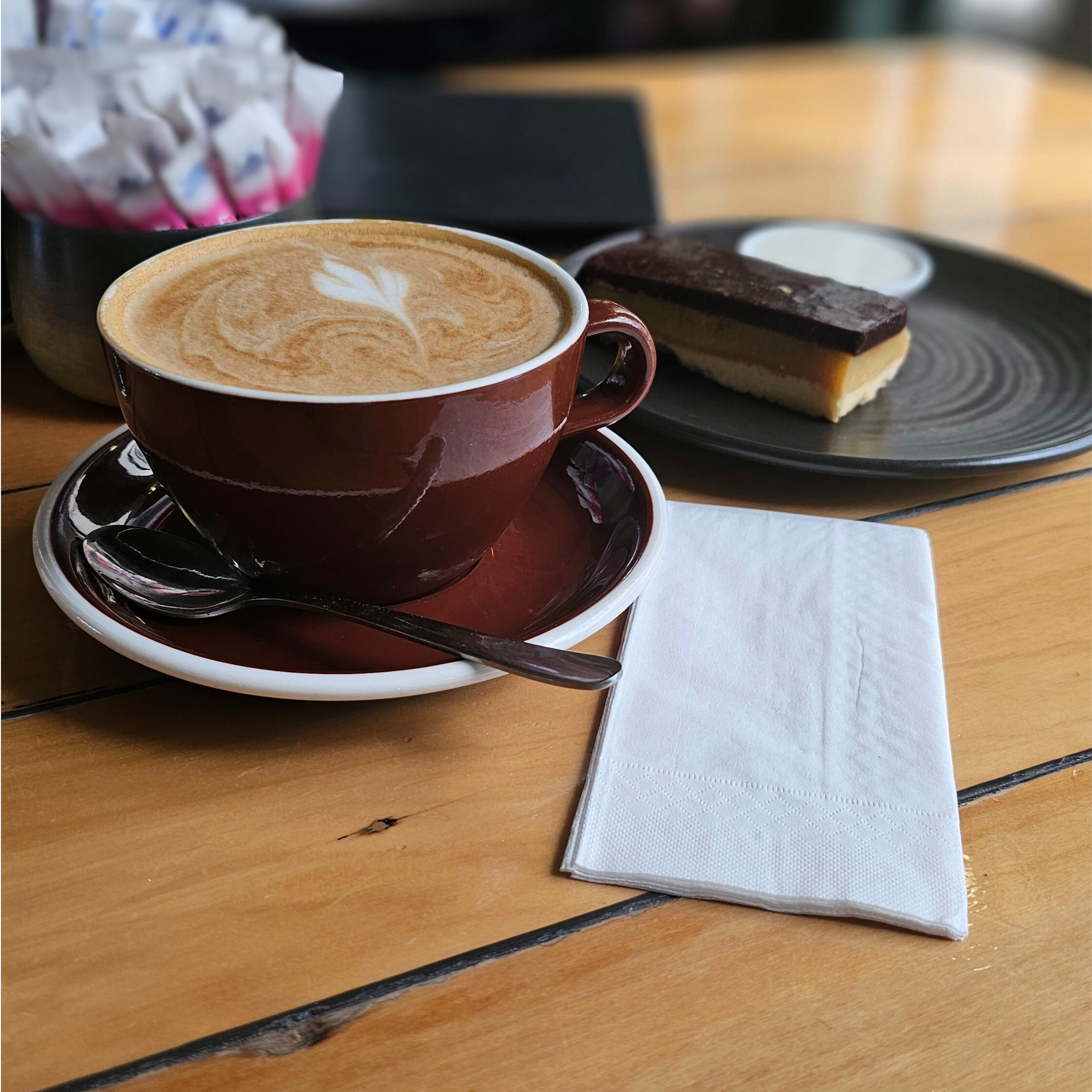 Flat white coffee and a slice sitting on a cafe table with a Green Choice 8th fold white napkin