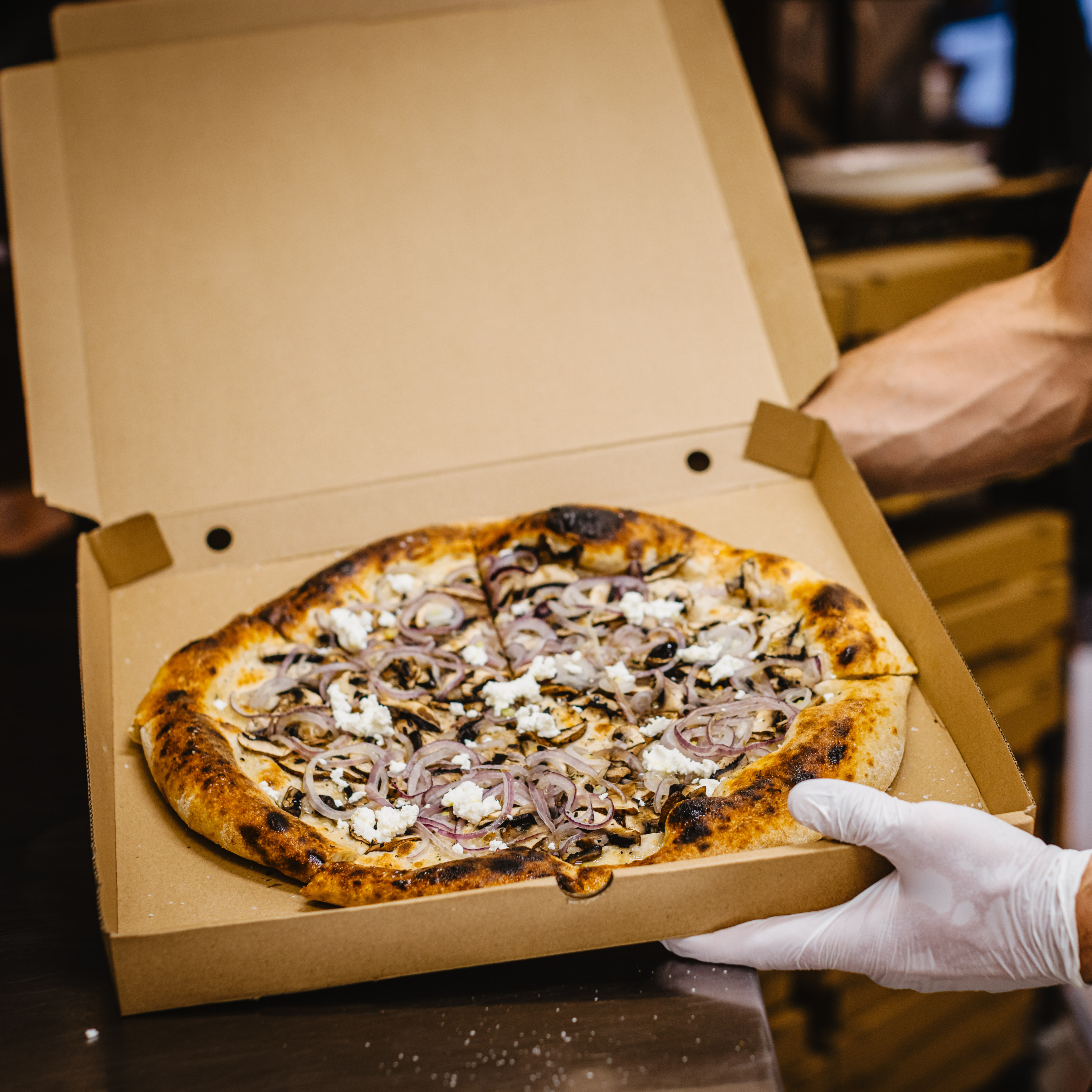 A close-up of a freshly baked pizza in a Green Choice brown pizza box