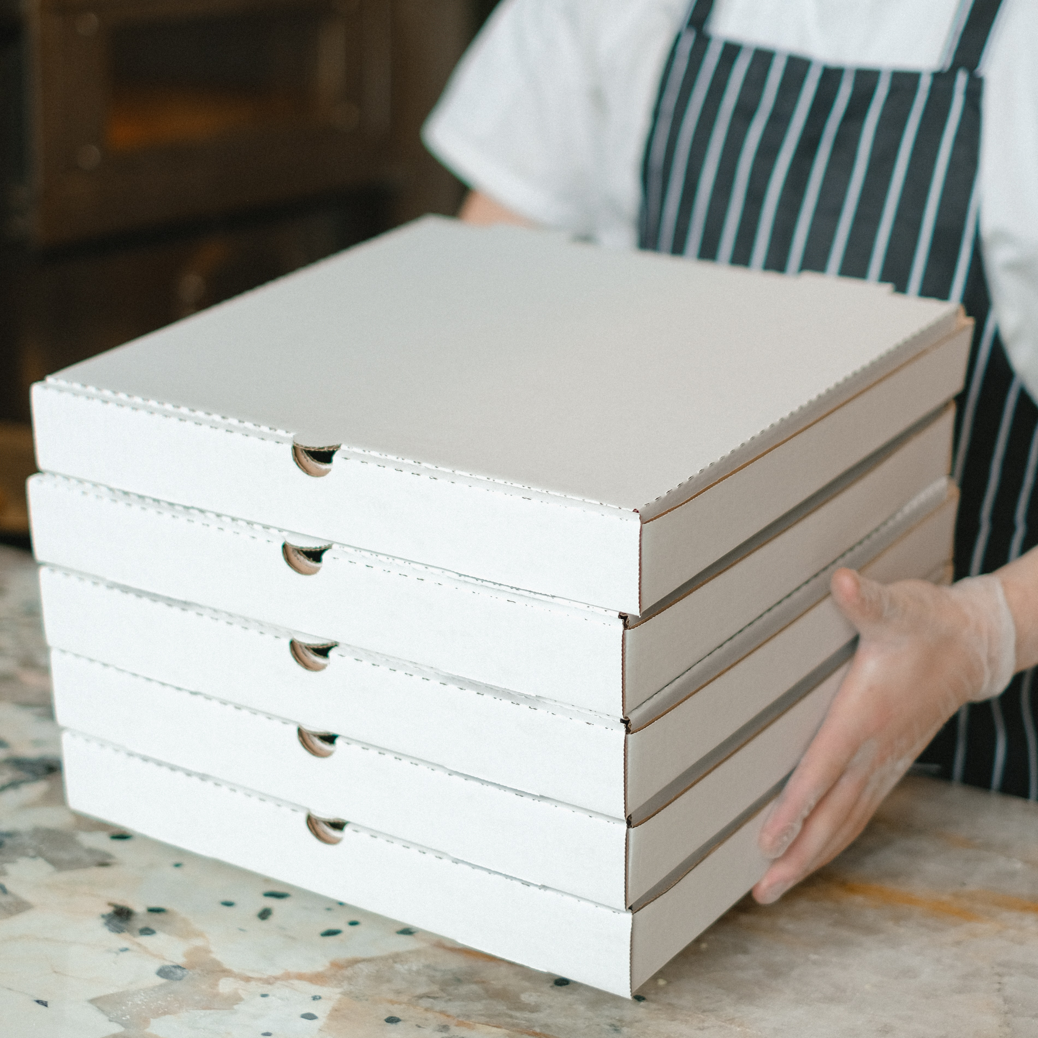 A close-up of a Pizza worker handing over a large order of pizzas