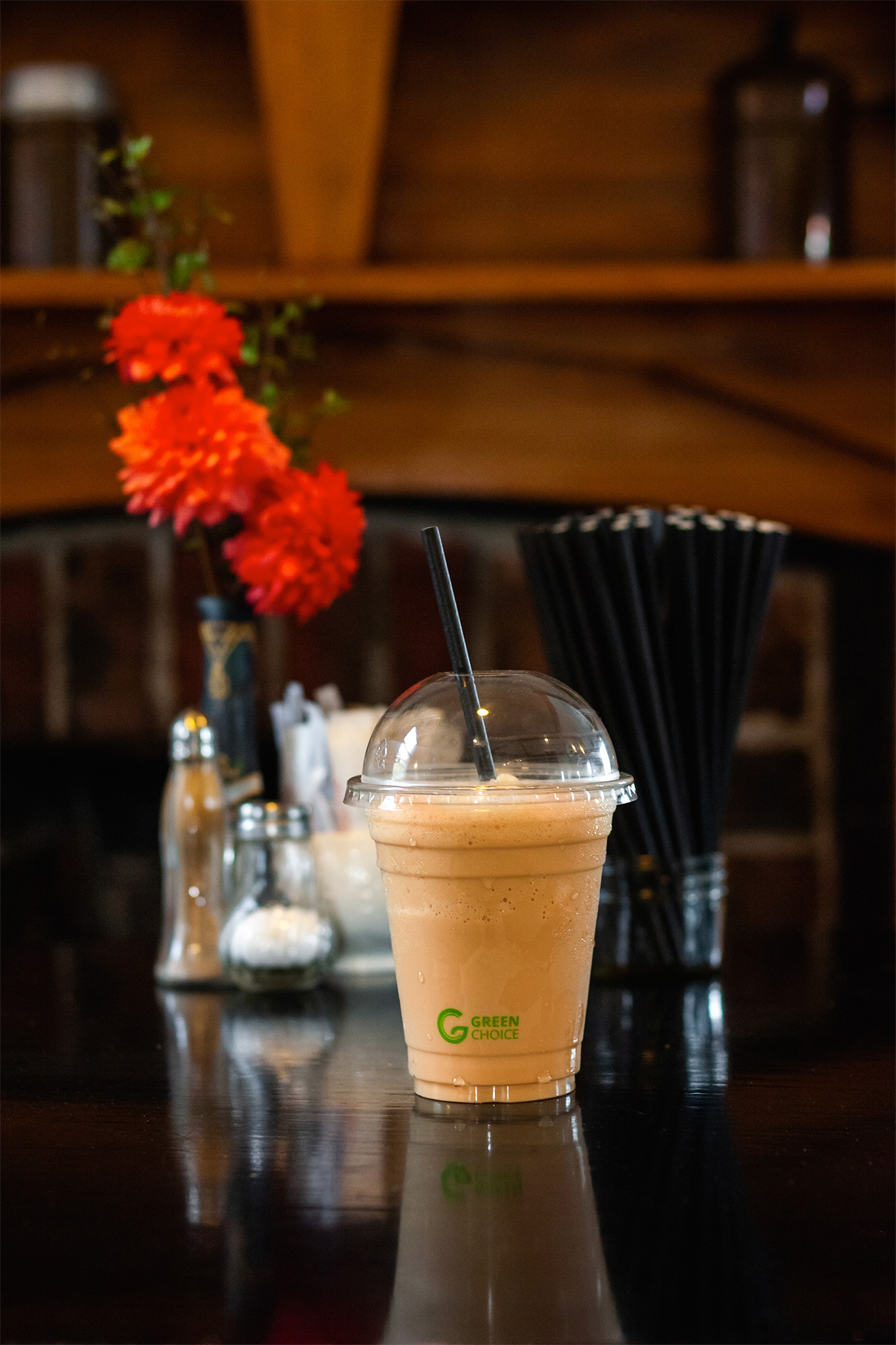 An iced coffee in a Green Choice Cold cup with a black paper straw, sitting on a cafe table