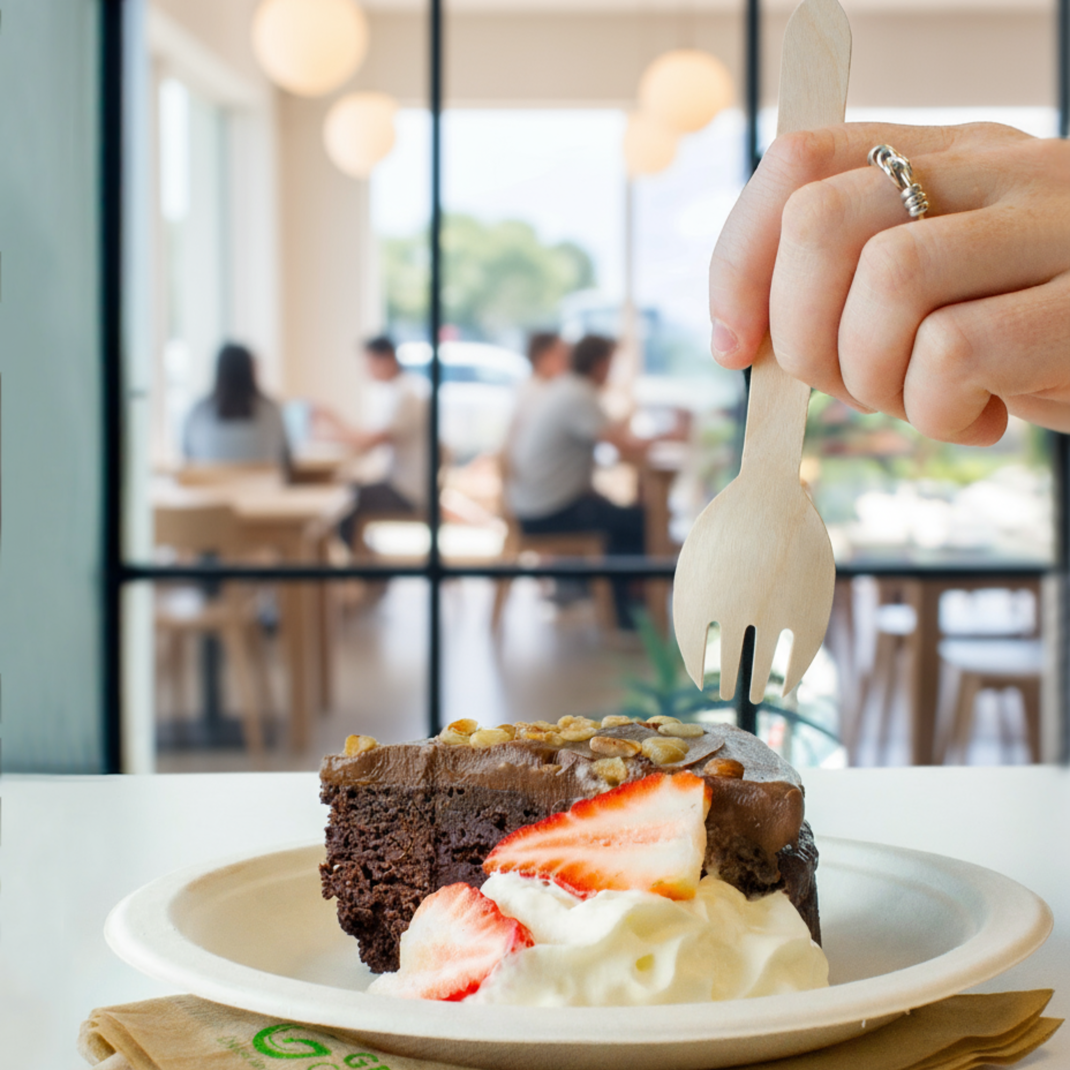 Lady using a spork to eat a slice of chocolate cake with whipped cream and strawberries