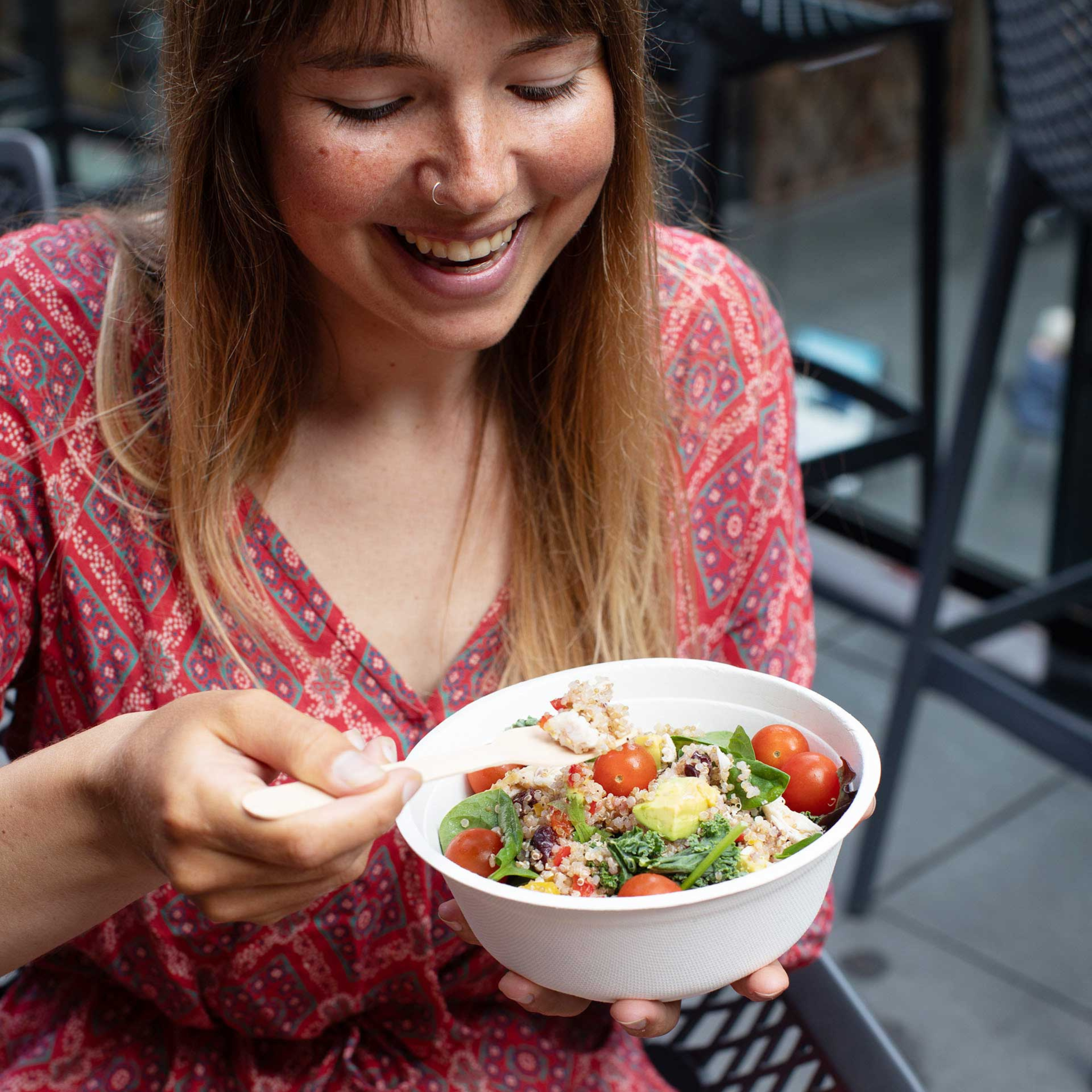 A lady sitting down, enjoying eating a salad from a Green Choice Sugar Cane Bowl