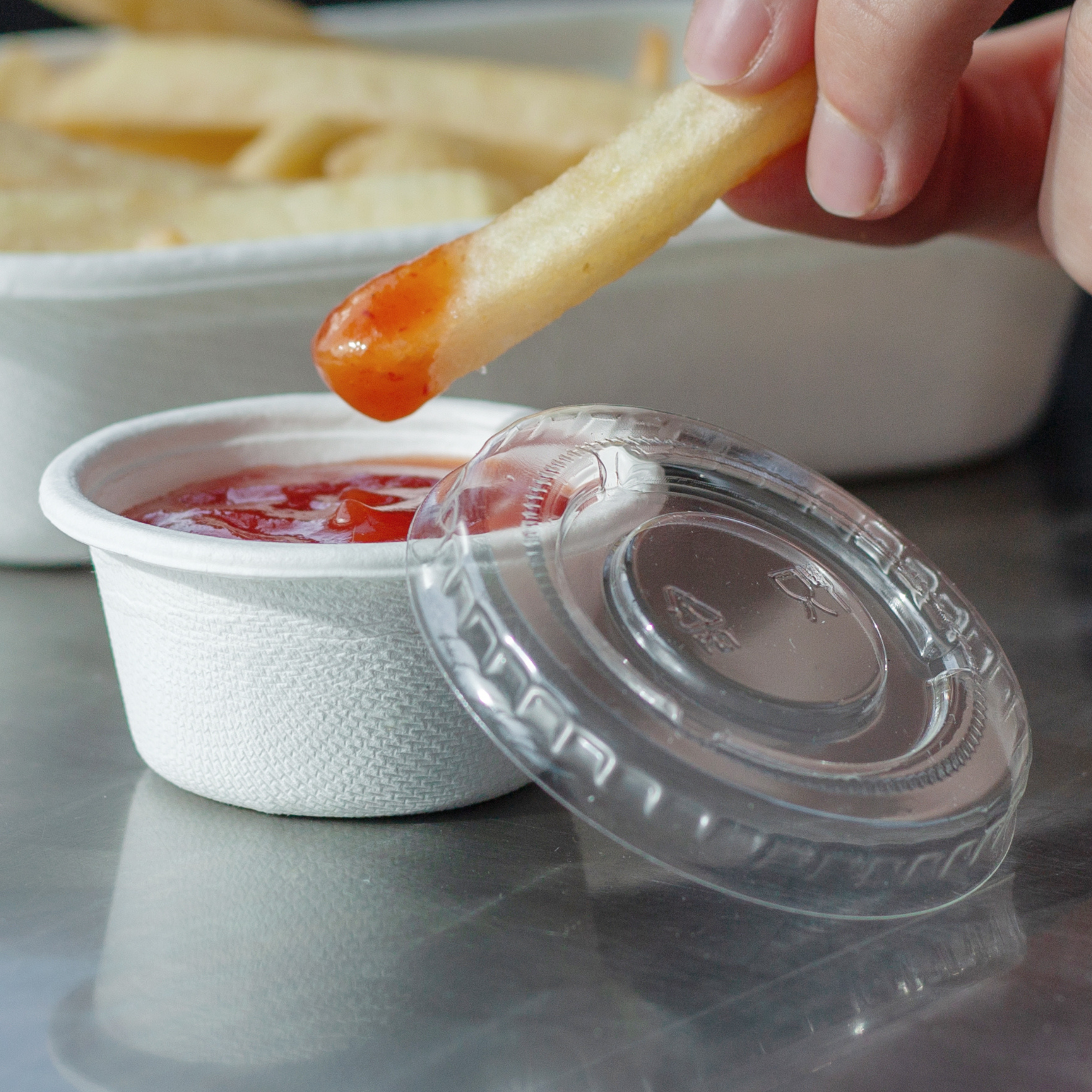 Close-up of someone dipping a chip into a Green Choice portion cup filled with sauce, with the lid leaning up against the cup