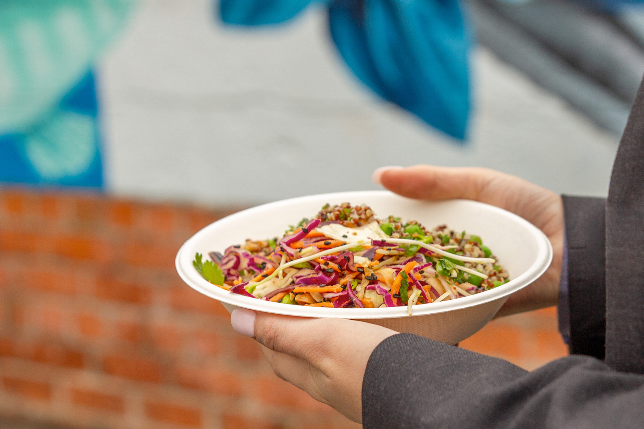 Close-up of a Green Choice desert bowl full of salad being carried next to a mural