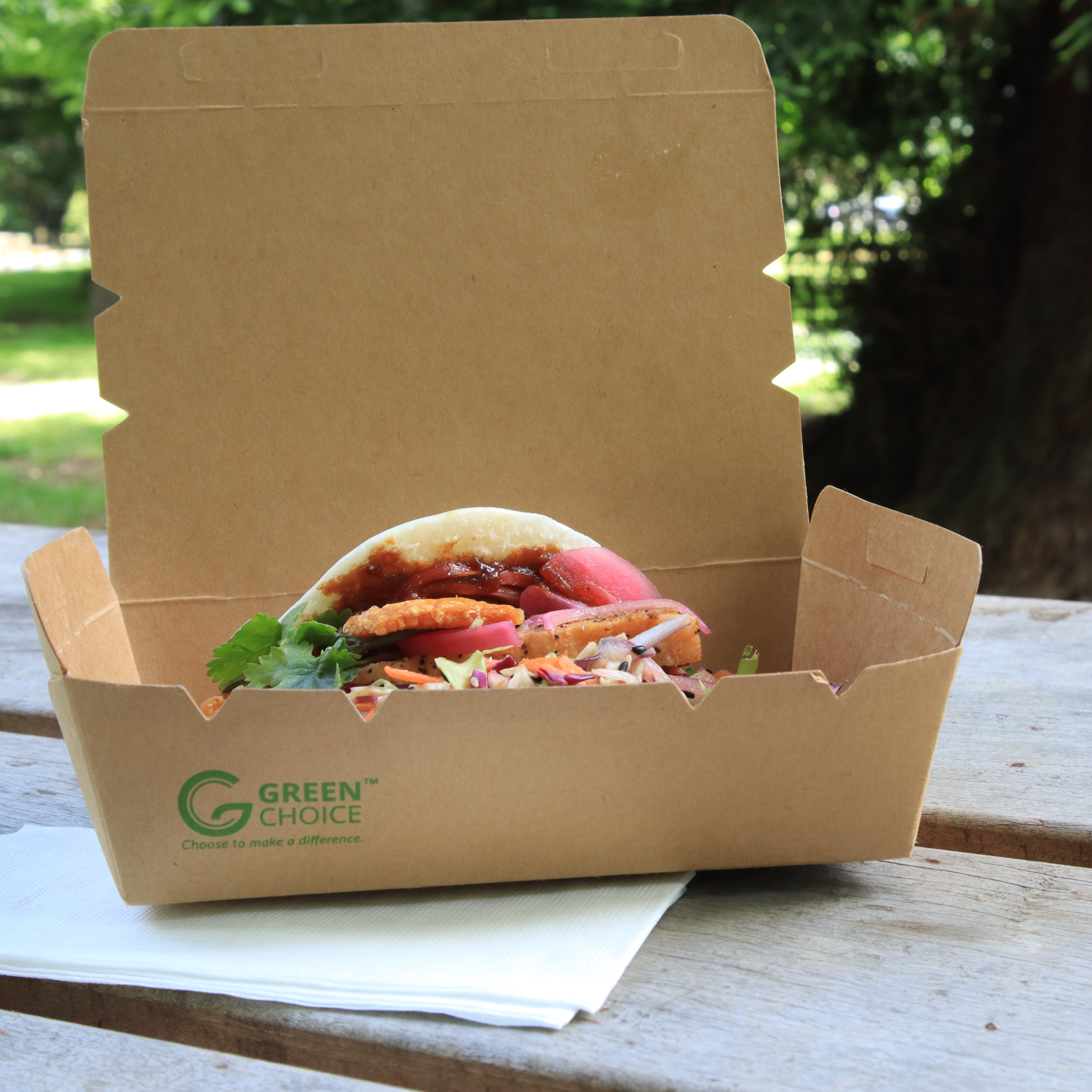 Green Choice takeaway container with a full bun sitting on an outdoor table