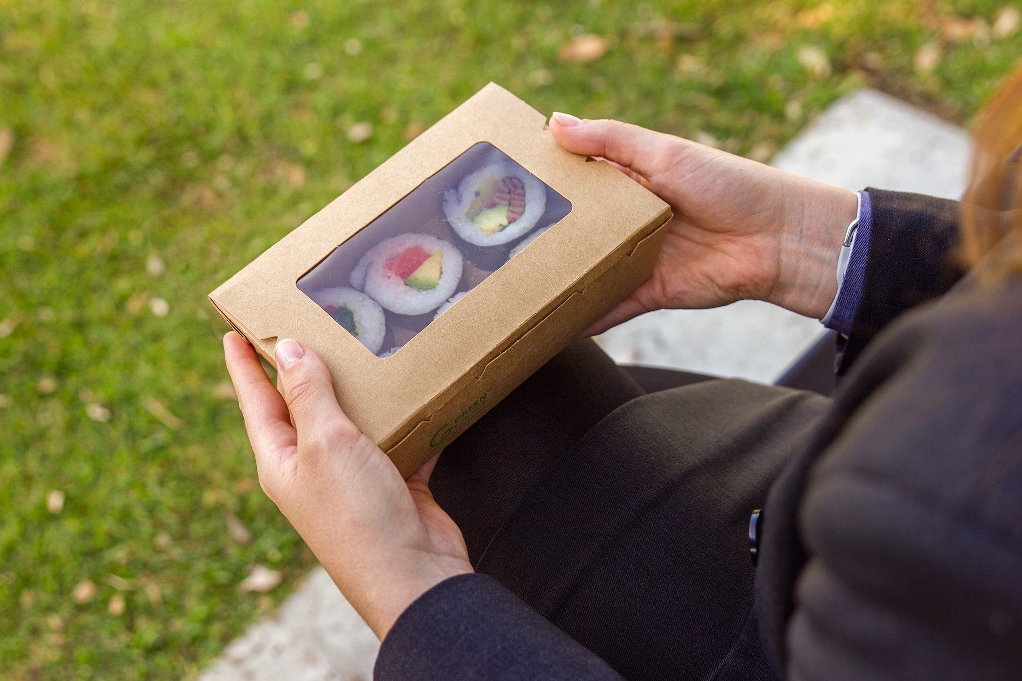 Lady holding a takeaway box with a window. You can see the contents of the sushi inside the Green Choice box
