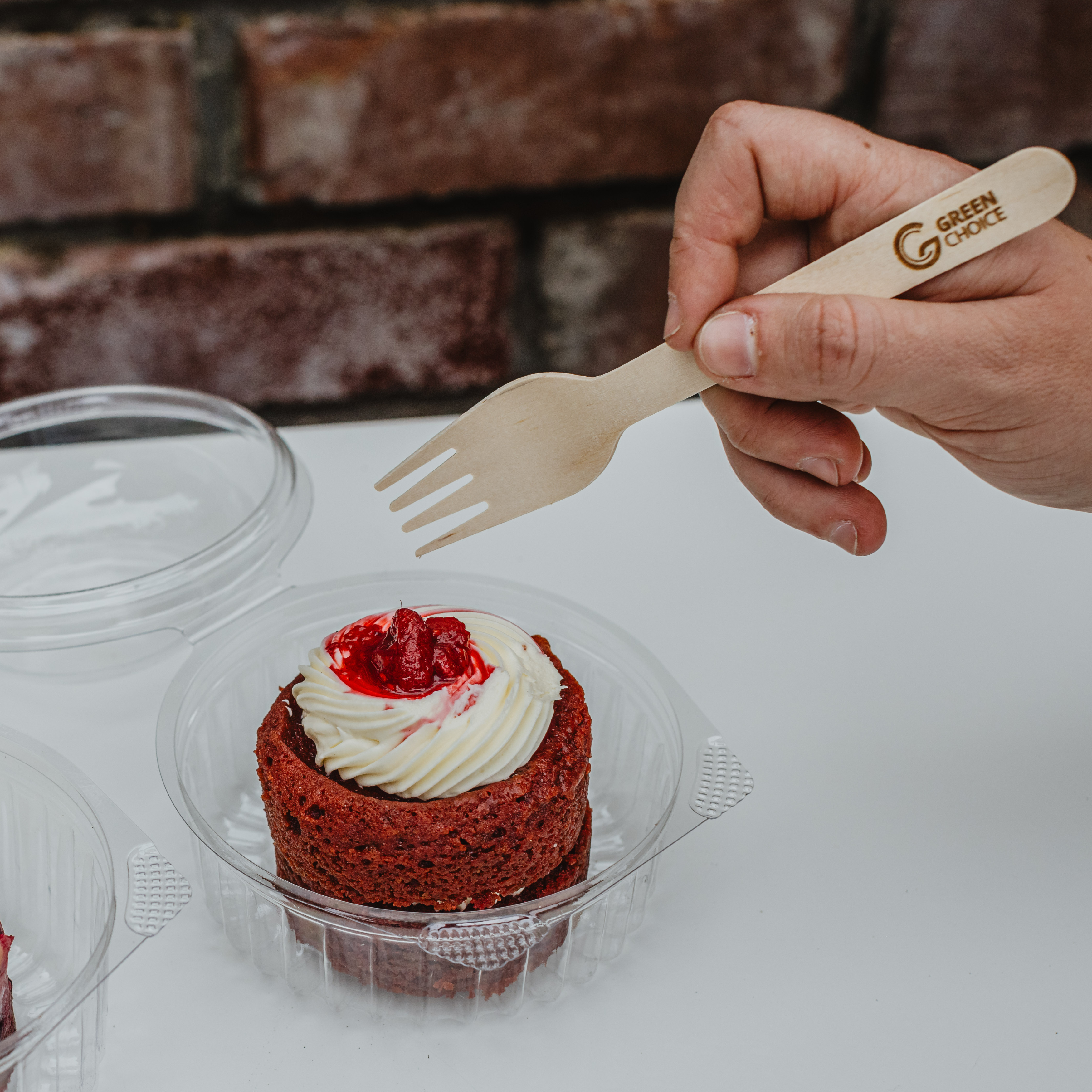 Someone holding a Green Choice Wooden Fork, ready to eat a red velvet cupcake from an Emperor Sho-Bowl