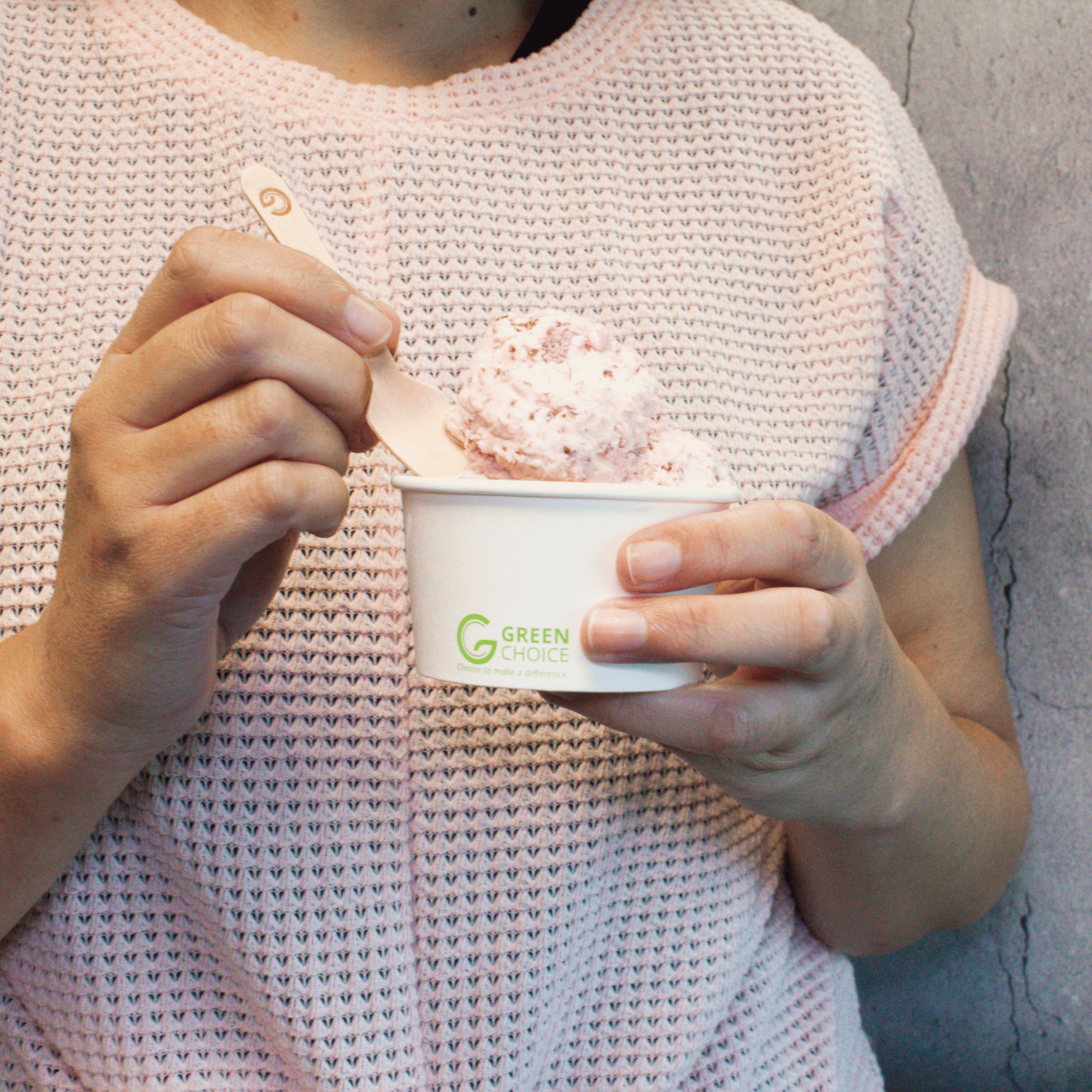 Lady holding a Green Choice dessert tub filled with strawberry ice cream, she is taking a spoonful of ice cream using a Green Choice Ice Cream Spoon