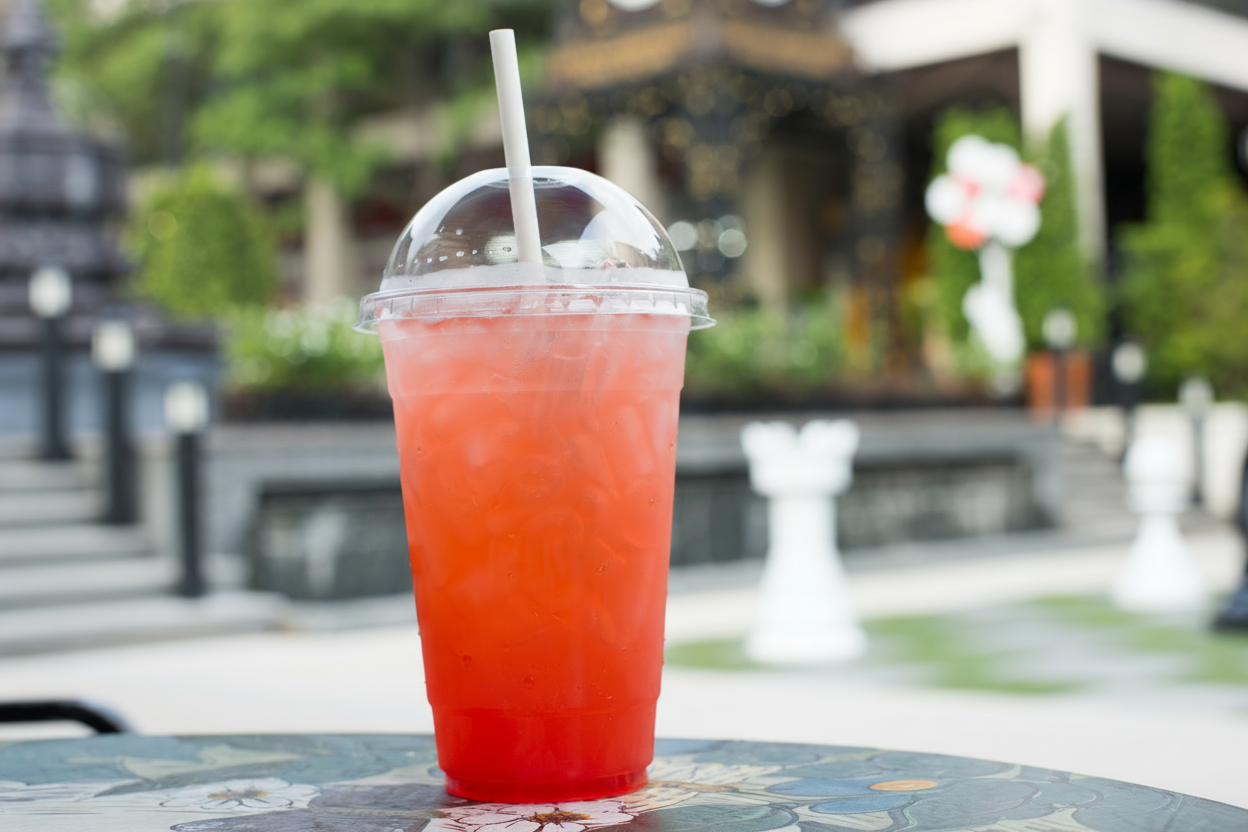 PET Clear Cup with dome lid  filled with pink iced drink and white straw on outdoor cafe table